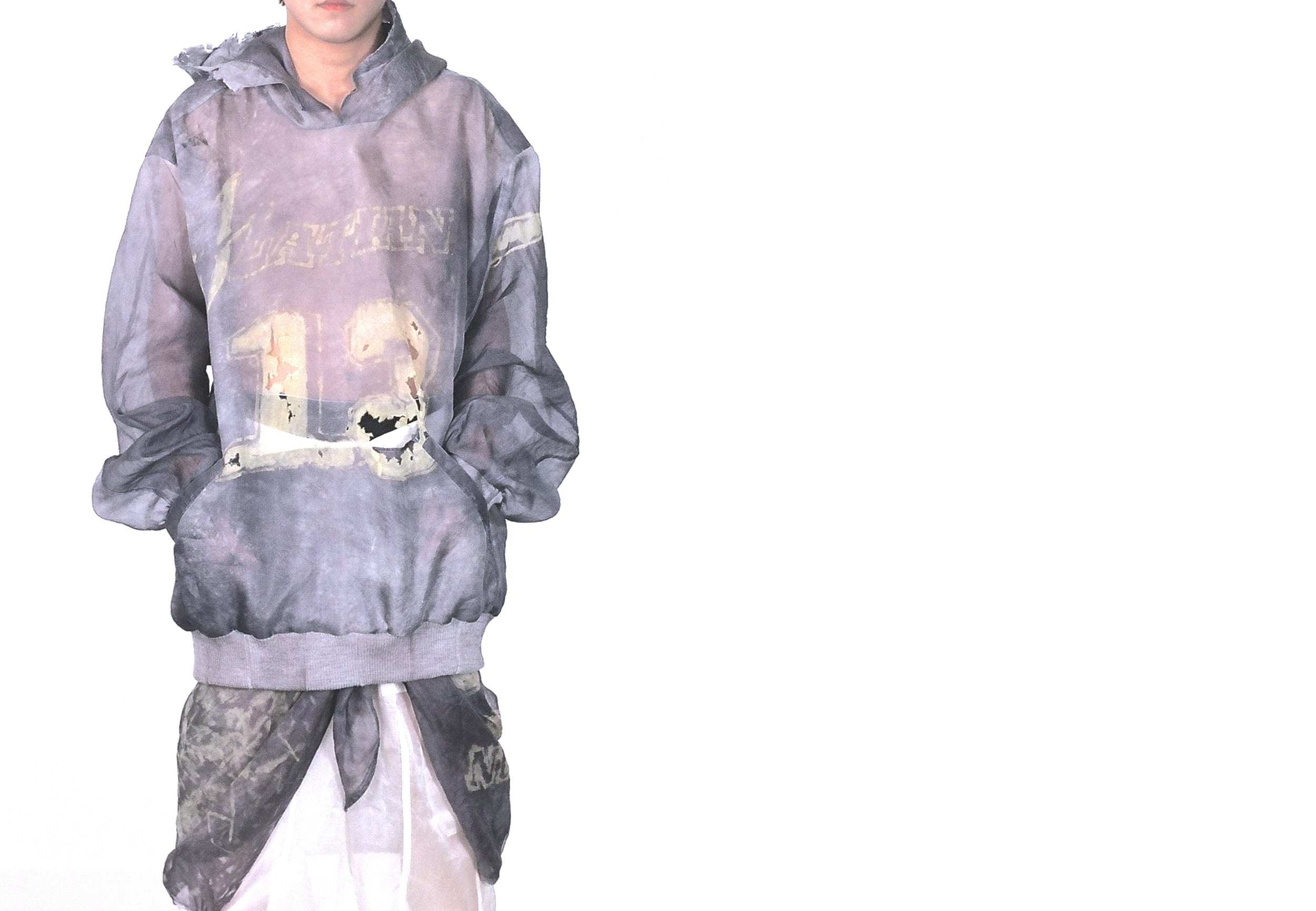 Person wearing a distressed oversized hoodie with a number and letters on the front, paired with layered pants, standing against a white background.