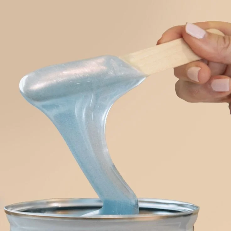 Person stirring wax in a wax machine, wearing a beige sweater and black glove.