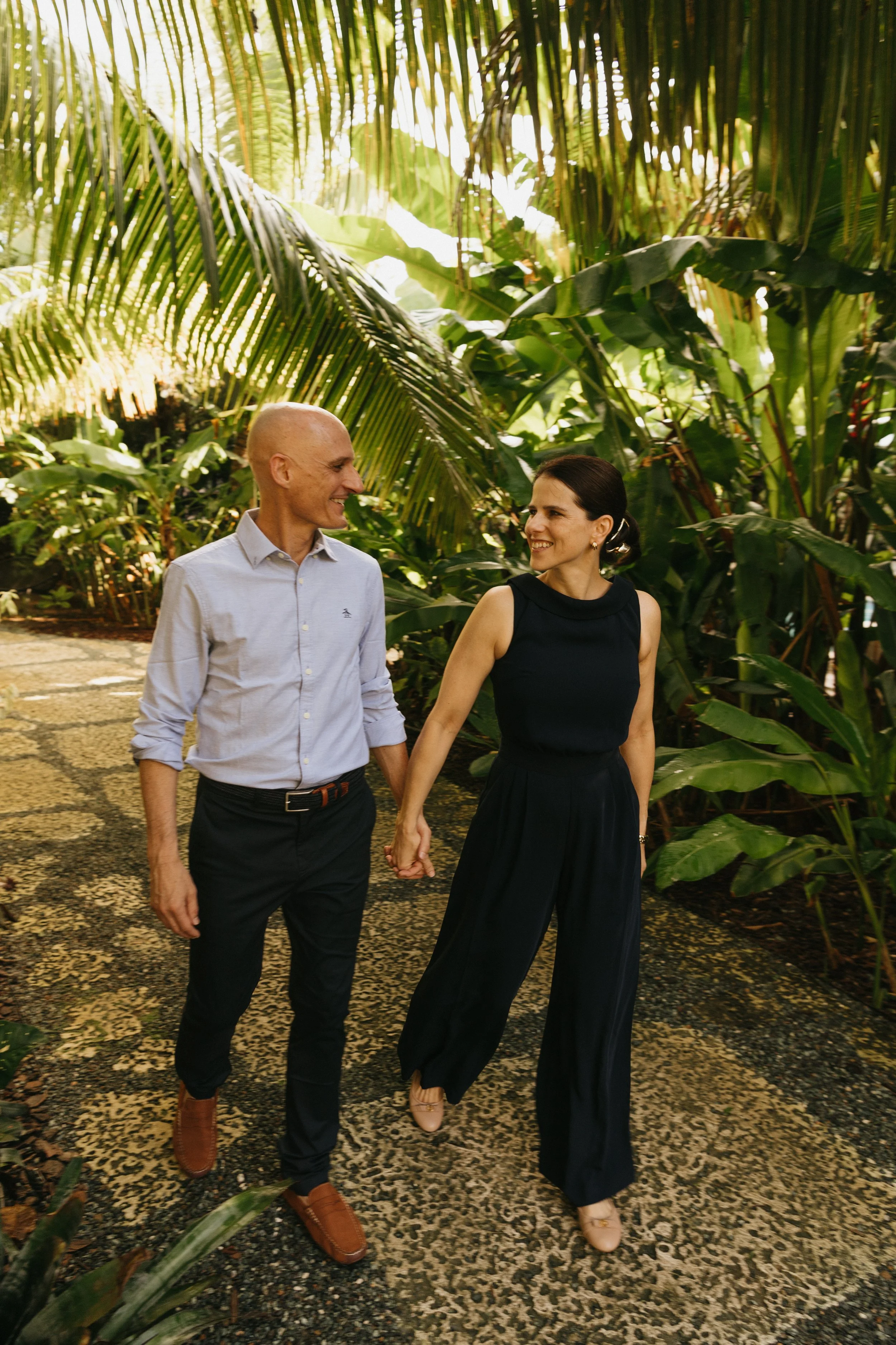 A husband and wife pair walking through The Hideaway Farm grounds among tropic palms overhead