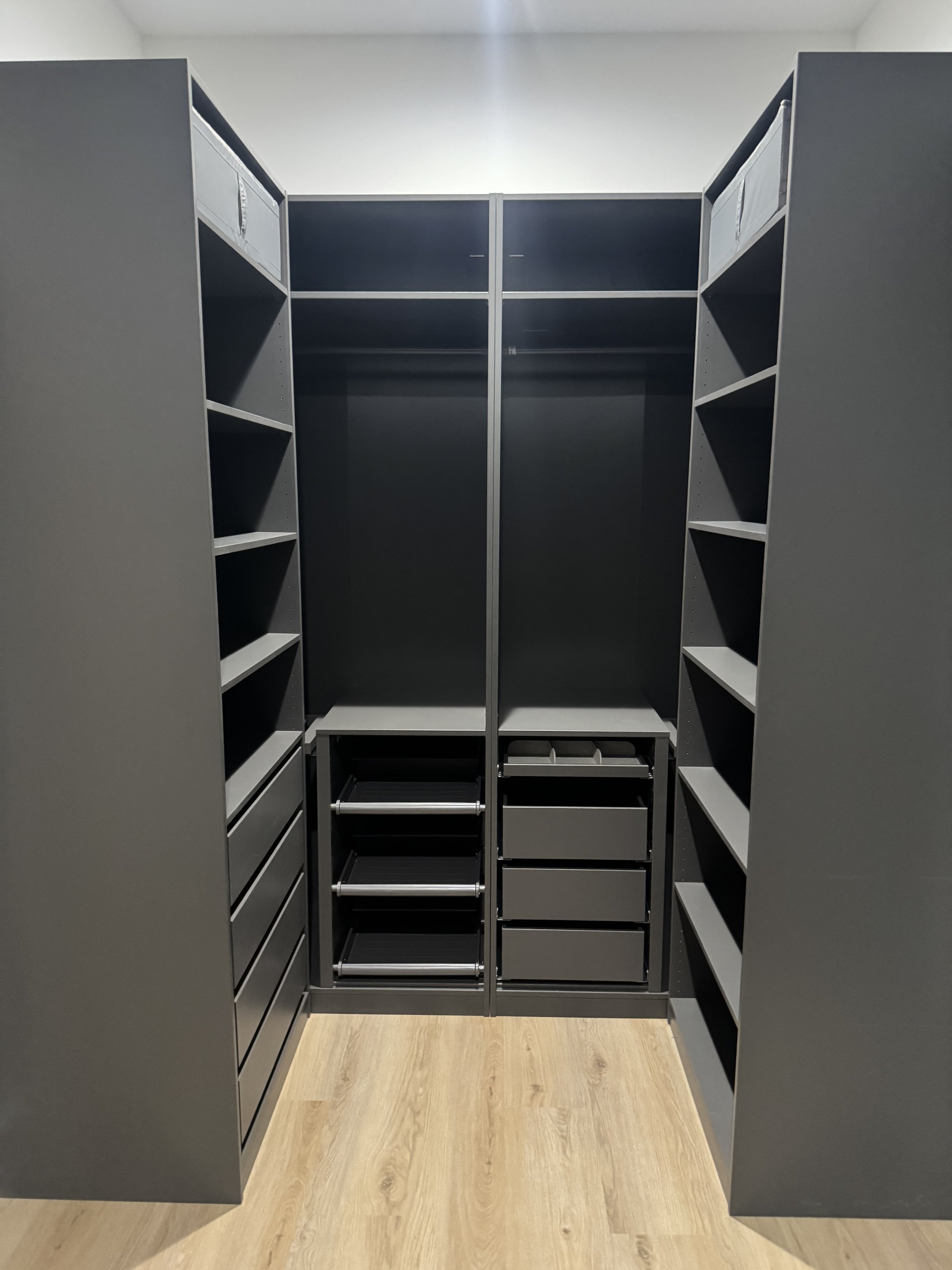 Empty walk-in closet with black shelving units, gold-colored wood flooring, and white walls.