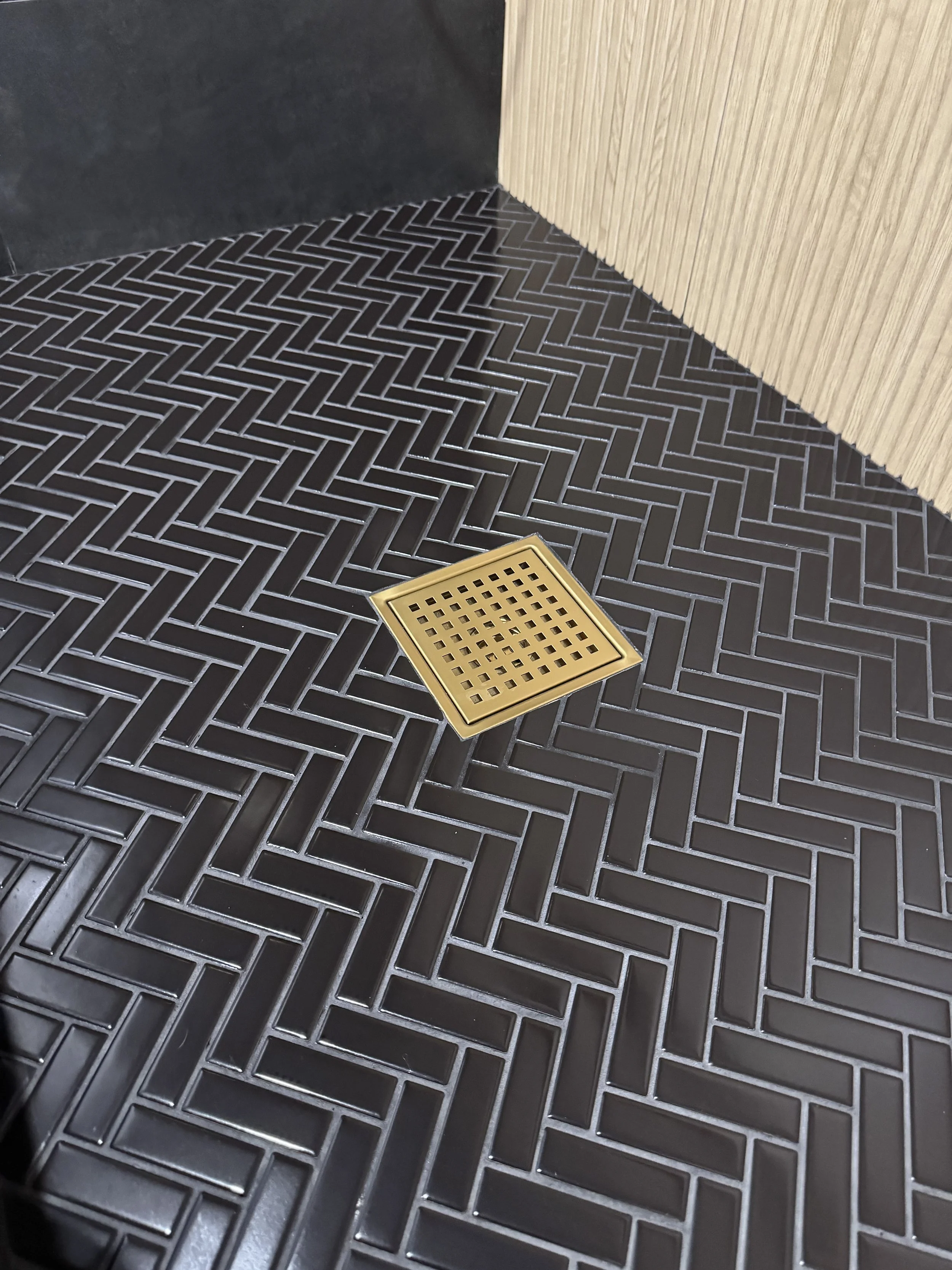 Black tiled floor with a gold square drainage grate and a wooden wall on the right side.