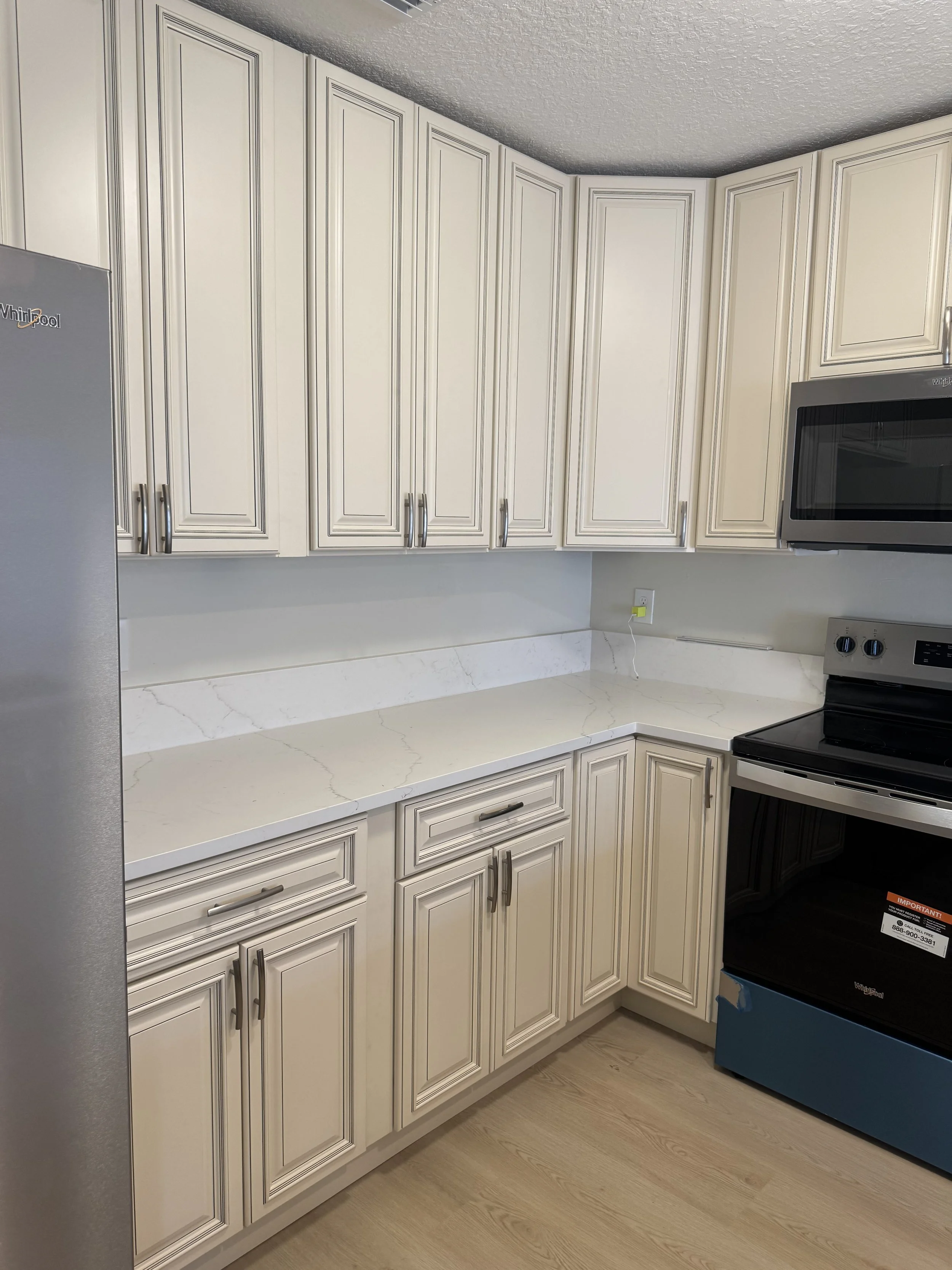 Kitchen with white cabinets, marble countertop, and black stove. Microwave above the stove, partially visible refrigerator on the left, and a power outlet on the wall.