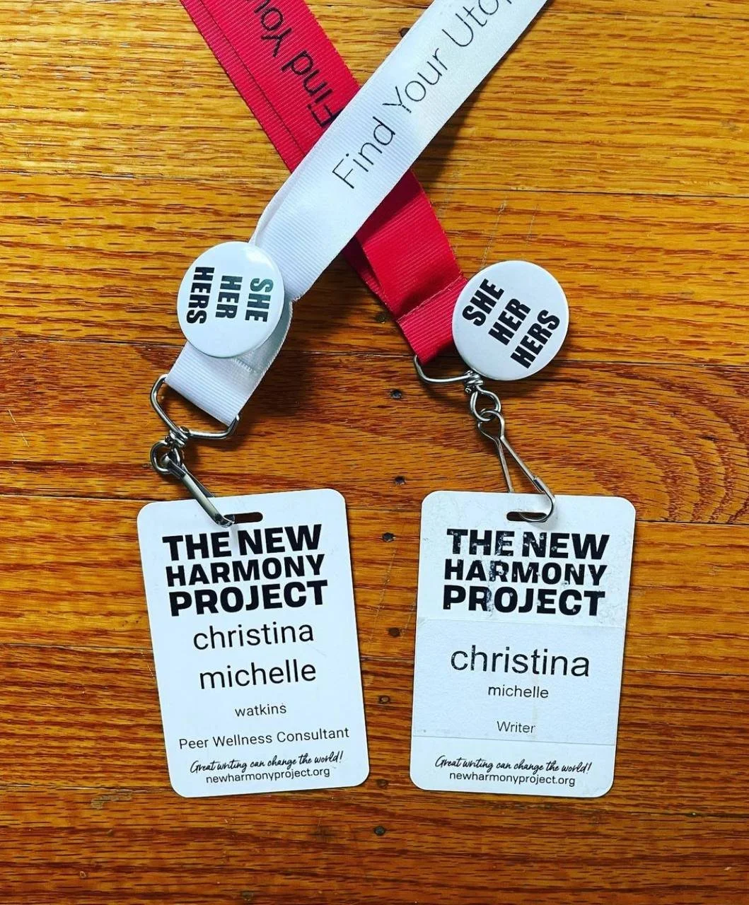 Picture of two lanyard name tags side by side: left one says " The New Harmony Project Christina Michelle Watkins, Peer Wellness Consultant" right one says The New Harmony Project: "Christina Michelle Writer".