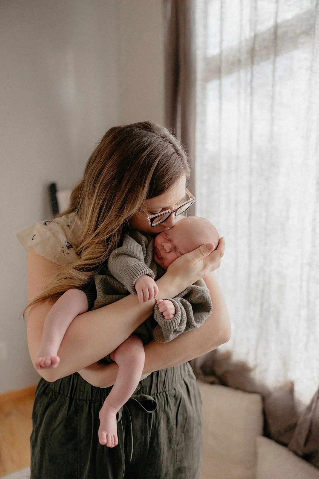 precious new mom kisses her newborn boy while holding him, letting the iowa city photographer arbor and light photograph them