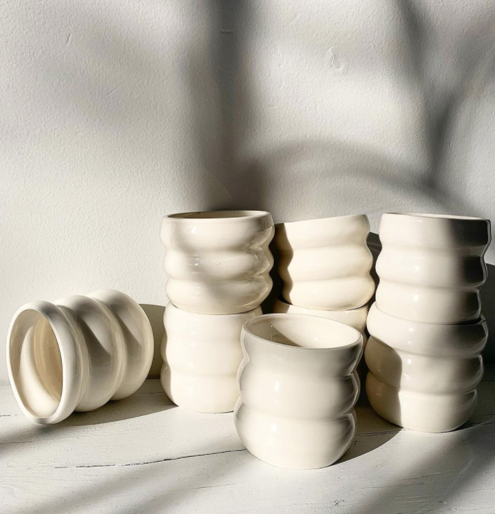 Plusieurs vases blancs en céramique avec une texture ondulée, disposés sur une surface blanche avec une lumière naturelle.