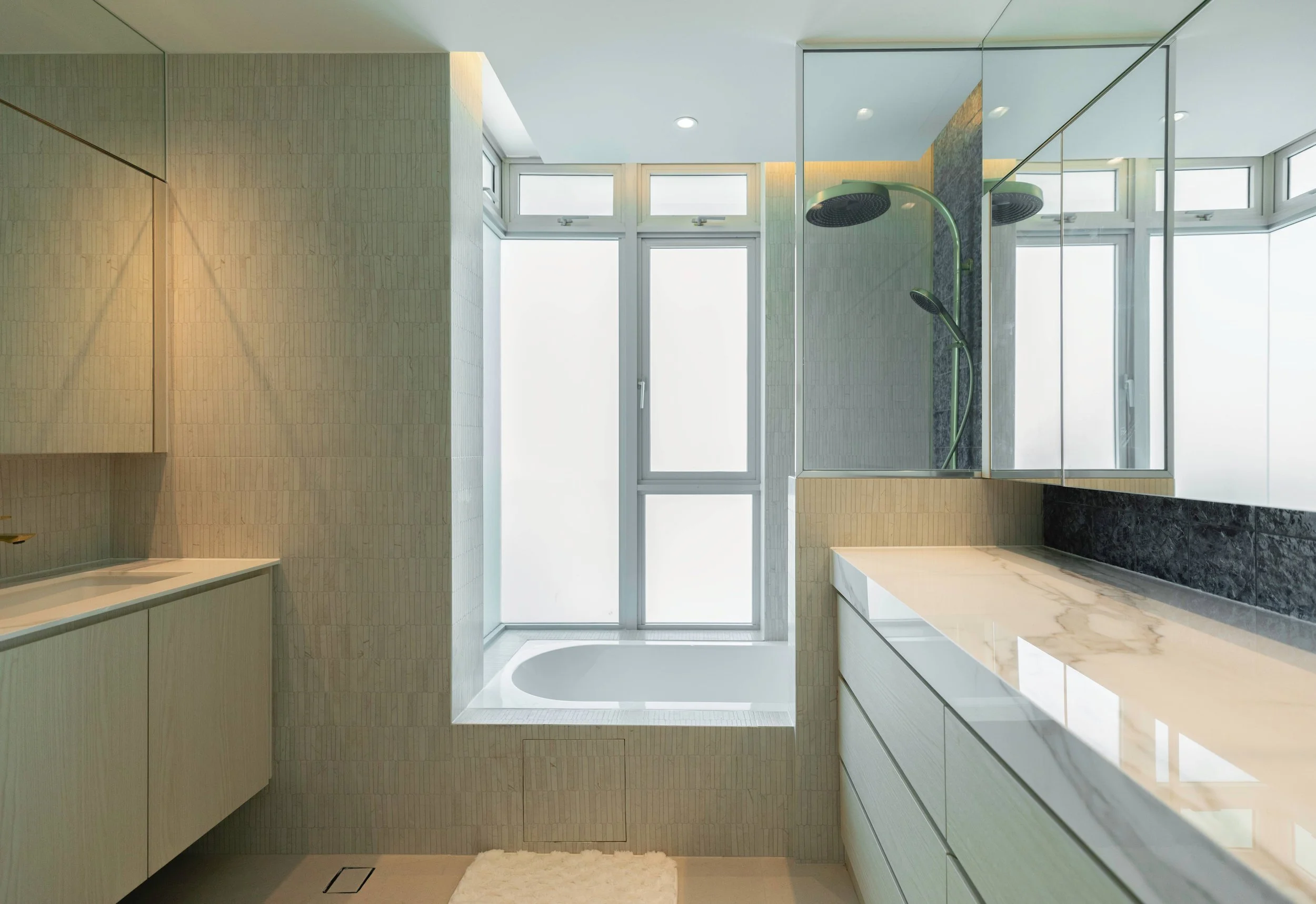 Modern bathroom with large window, shower area with black showerheads, beige and black tiled walls, white marble countertop, and a mirror reflecting the space.