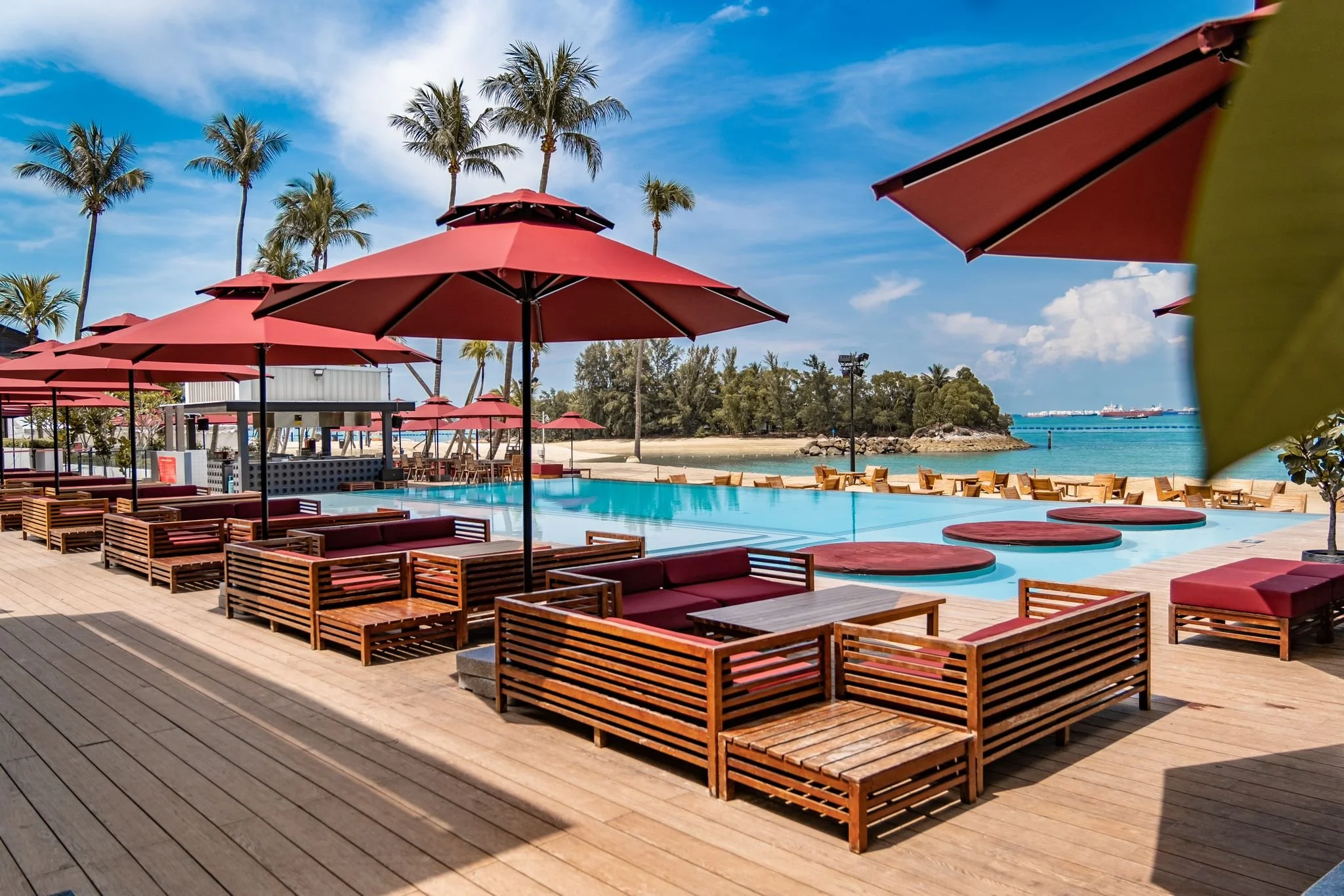 Outdoor beachfront setting at Rumours Beach Club Sentosa with tropical landscaping, casual seating and seaside atmosphere