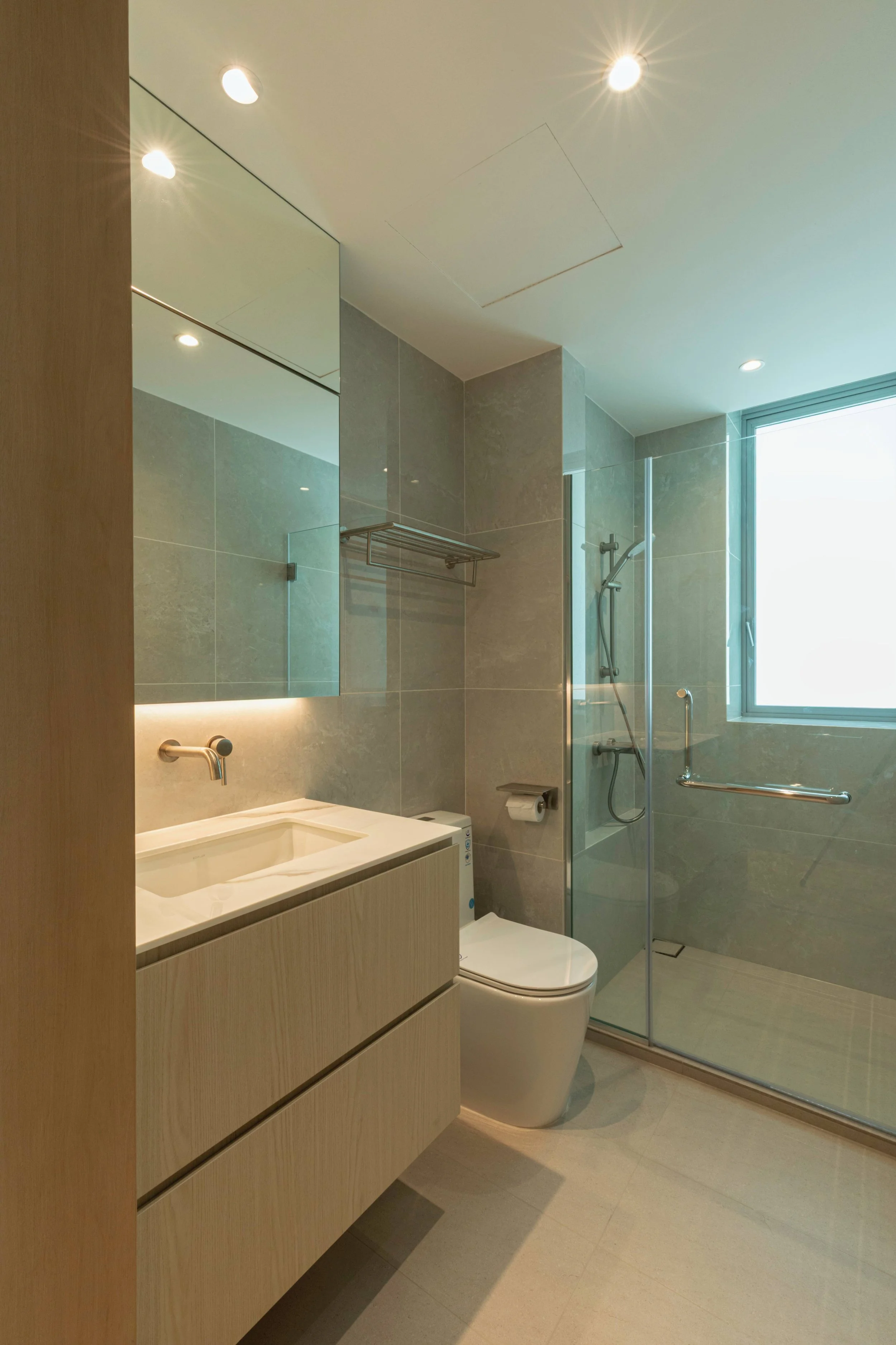 Modern bathroom with a wooden vanity, white sink, wall-mounted faucet, toilet, tiled walls, a glass-enclosed shower with a handheld showerhead, a large window, and recessed ceiling lights.