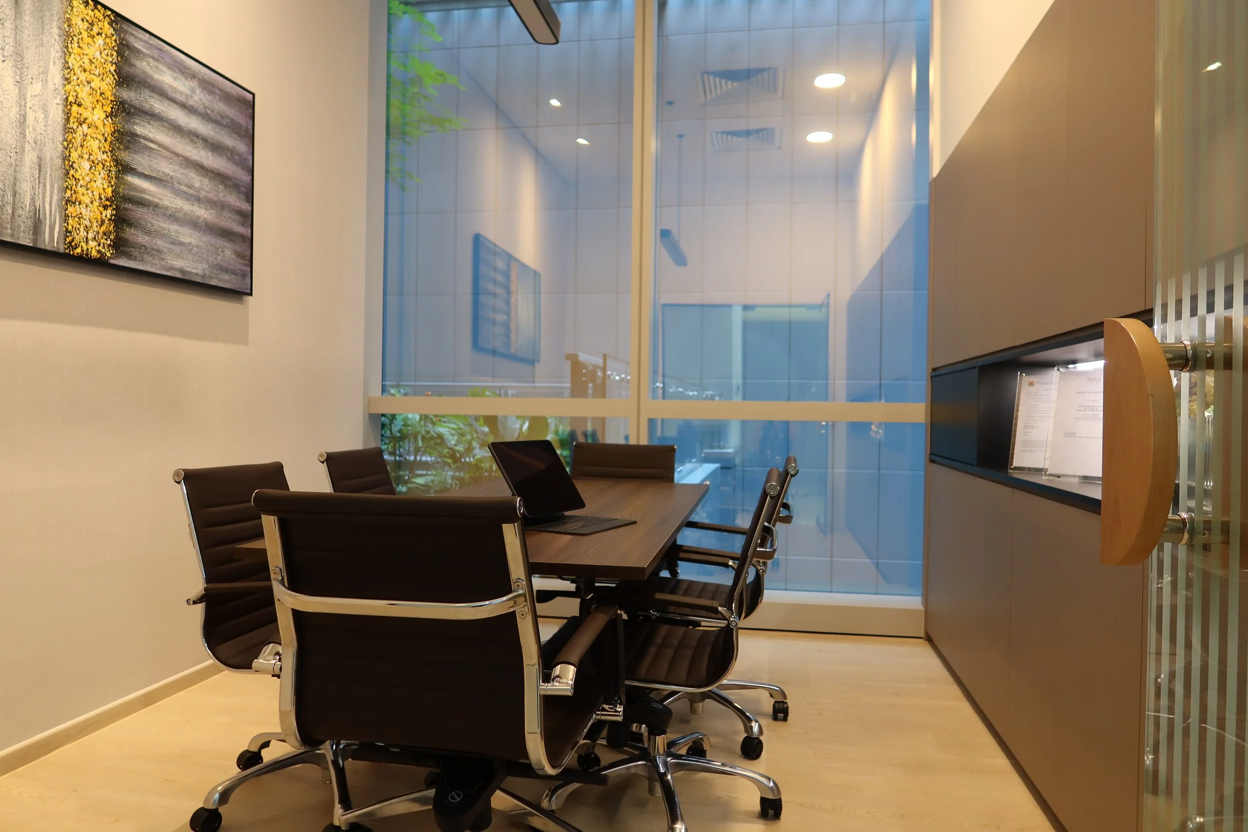 Modern conference room with a long wooden table, black and brown chairs, and decorative items on a black shelf against a beige wall.
