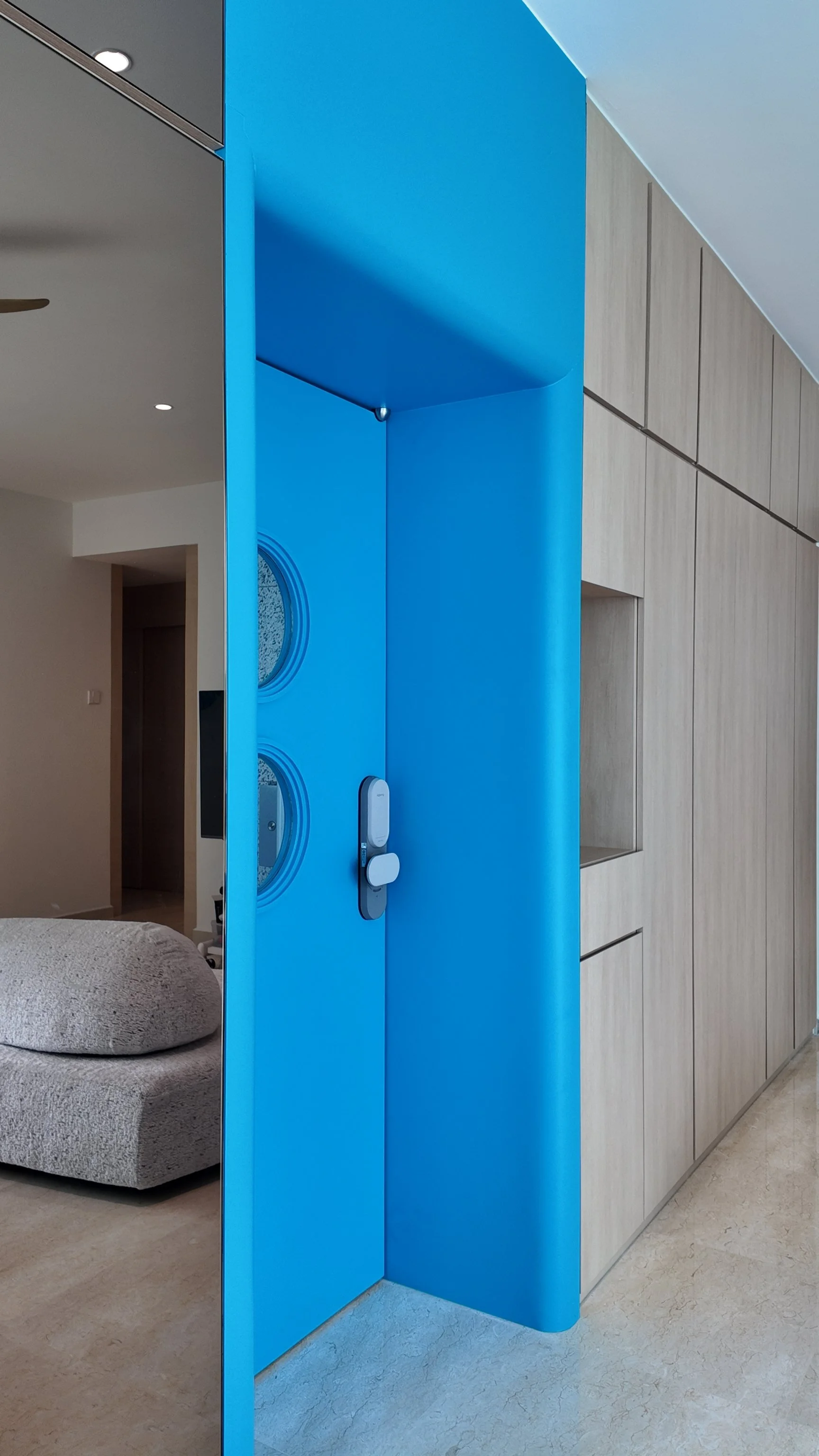 A modern interior featuring a blue sliding door with circular windows, a gray textured chair, and light wood cabinetry.