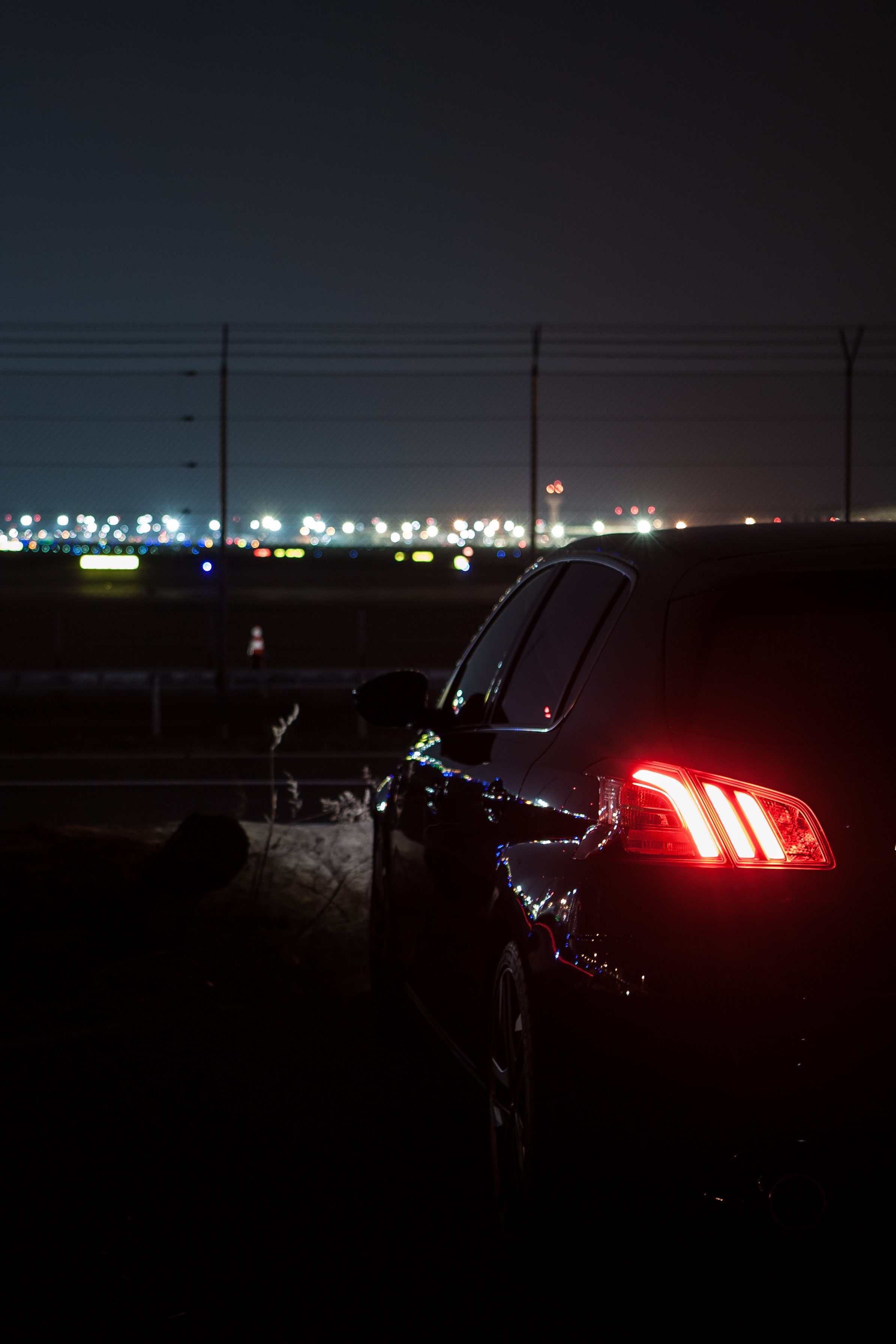 Auto bei Nacht mit eingeschaltetem Rücklicht am Flughafen, Lichter im Hintergrund.