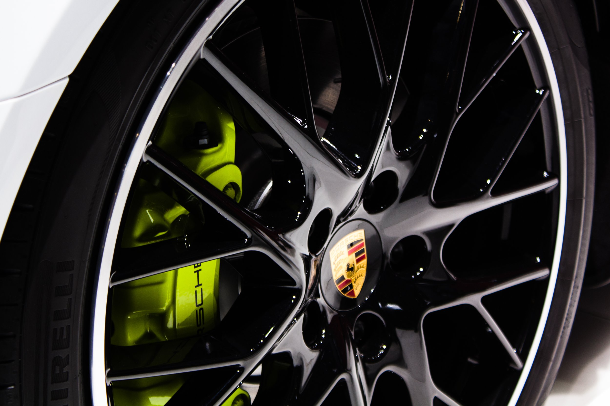 Schwarze Autofelge mit grünem Bremssattel und Porsche-Emblem, Reifenaufschrift "Pirelli" sichtbar.