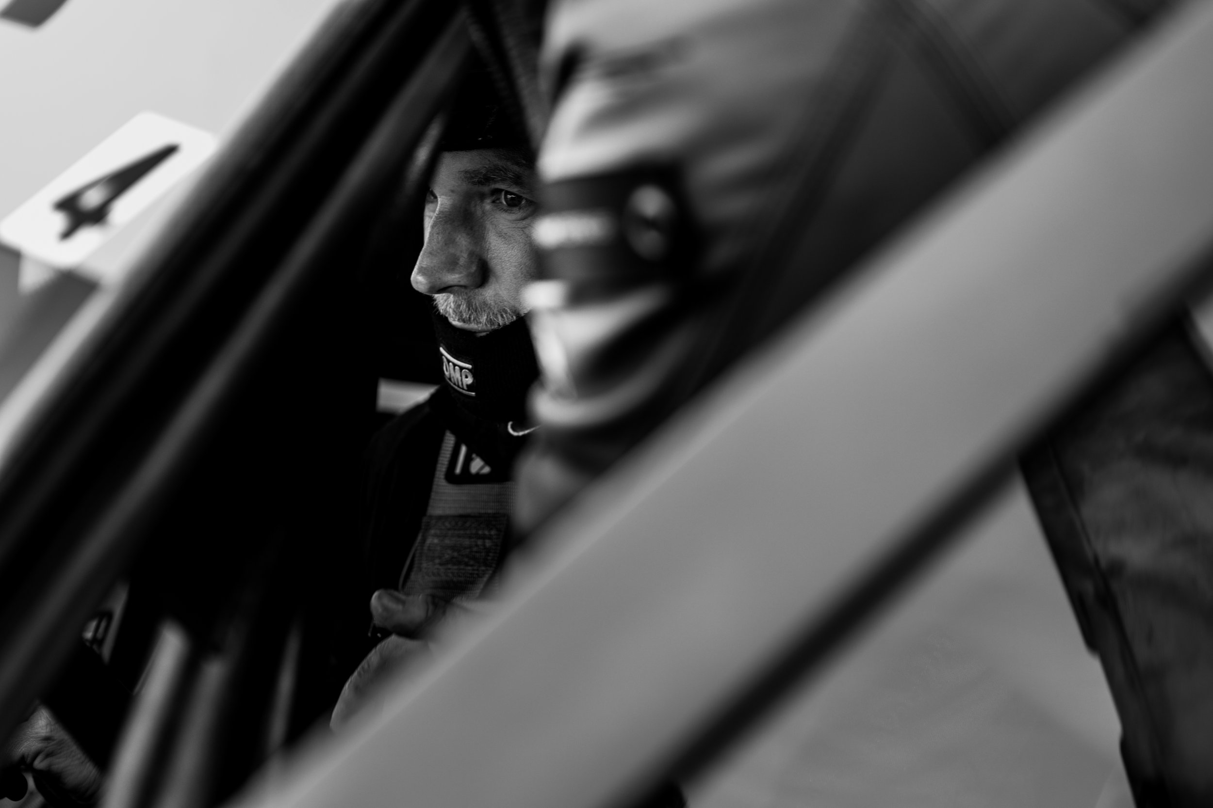 Schwarz-weiß-Foto eines konzentrierten Rennfahrers mit Helm und Sicherheitsgurt im Auto. Seitenansicht durch Fenster fotografiert.