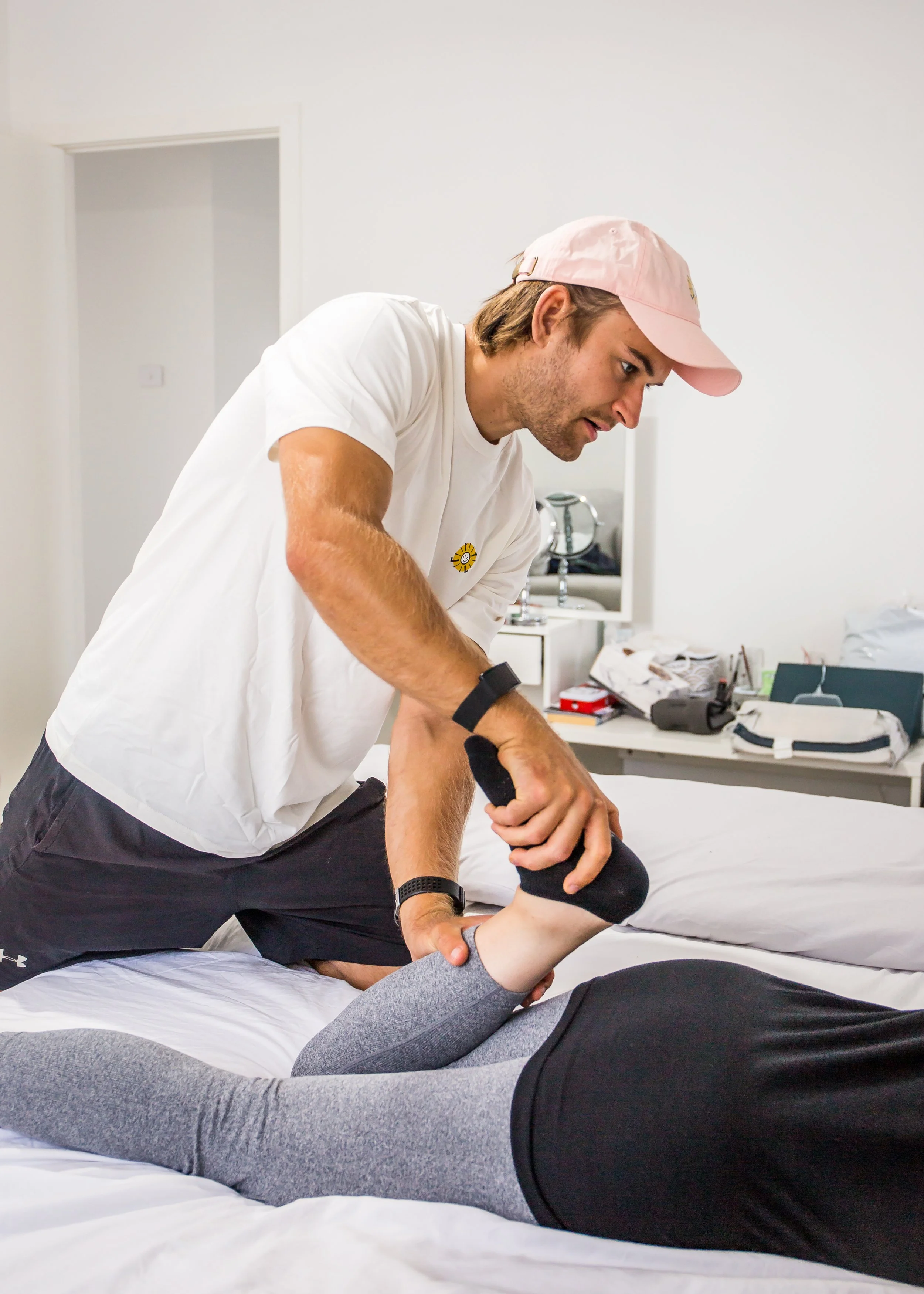 A man providing physical therapy to a woman lying on a bed, stretching her leg.
