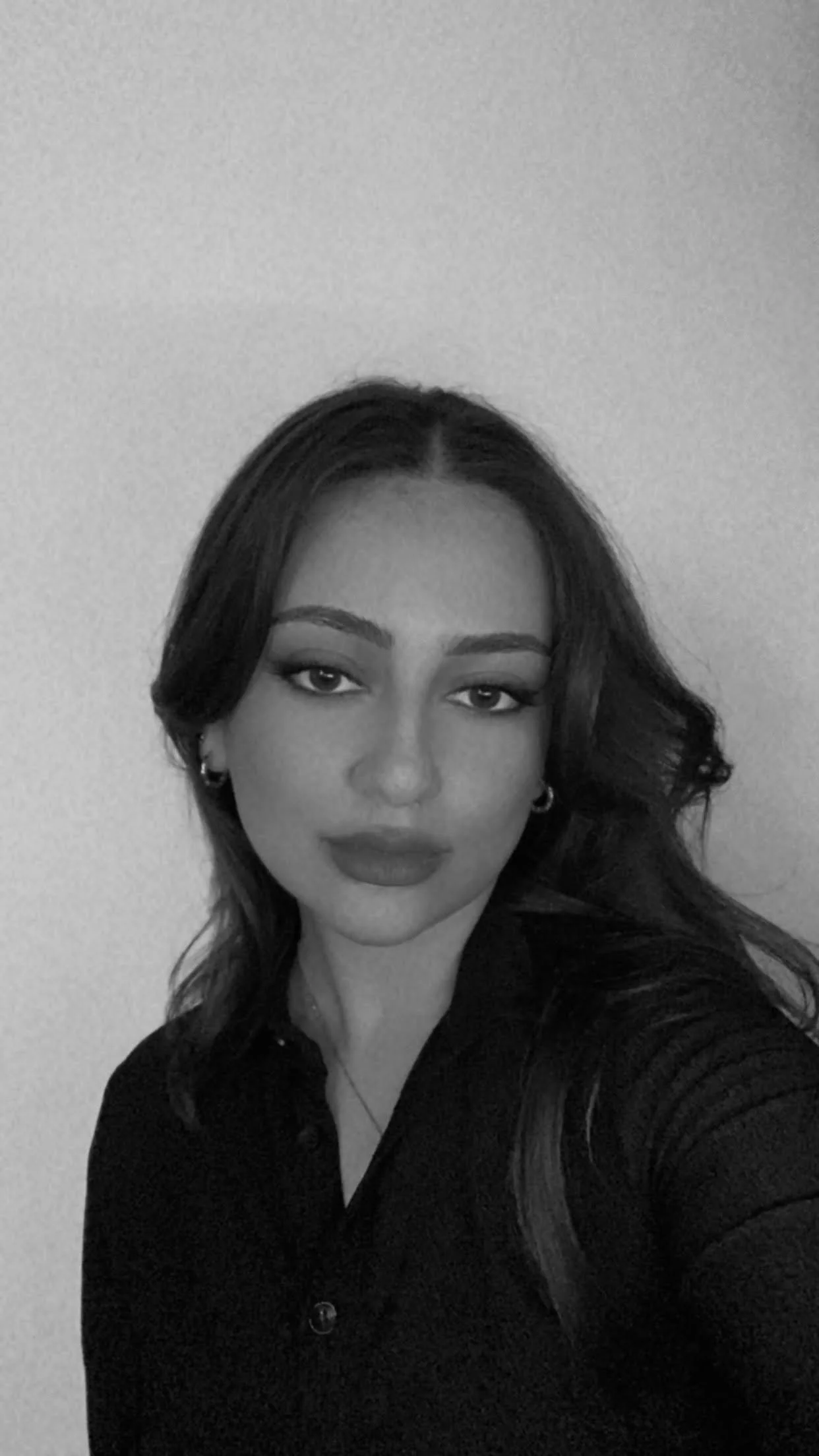 Black and white portrait of a woman with dark hair, eyes, and makeup, wearing a dark top and earrings.