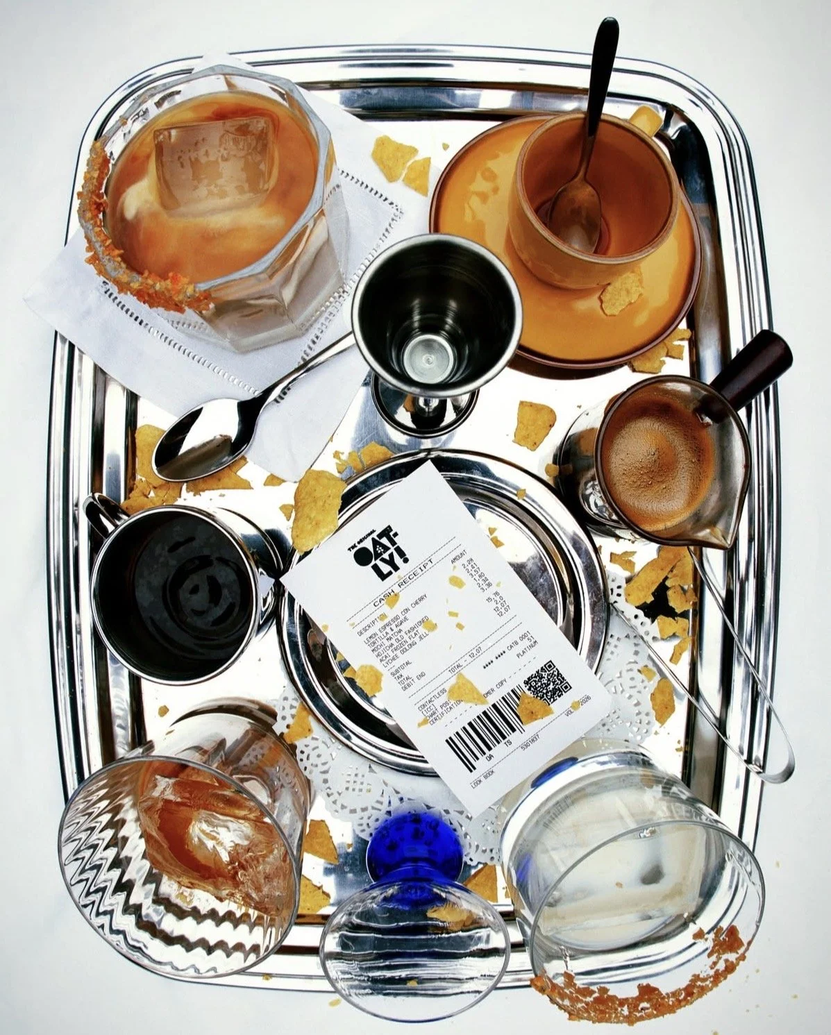 Empty food tray with spilled chips, a crumpled receipts, various used glasses, and remnants of food around.