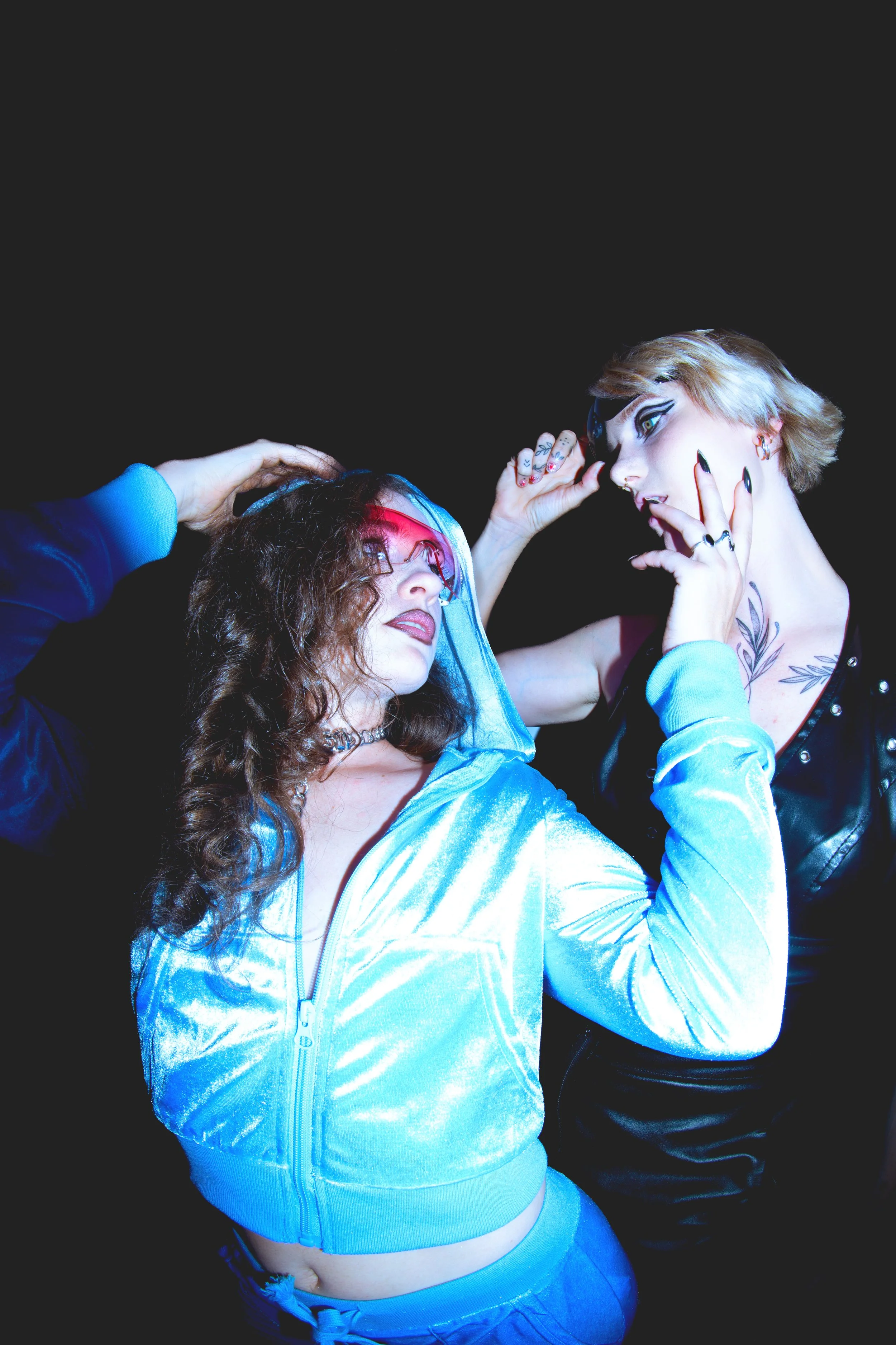 Deux femmes posant de manière expressive dans un fond noir, portant des vêtements modernes et stylés.