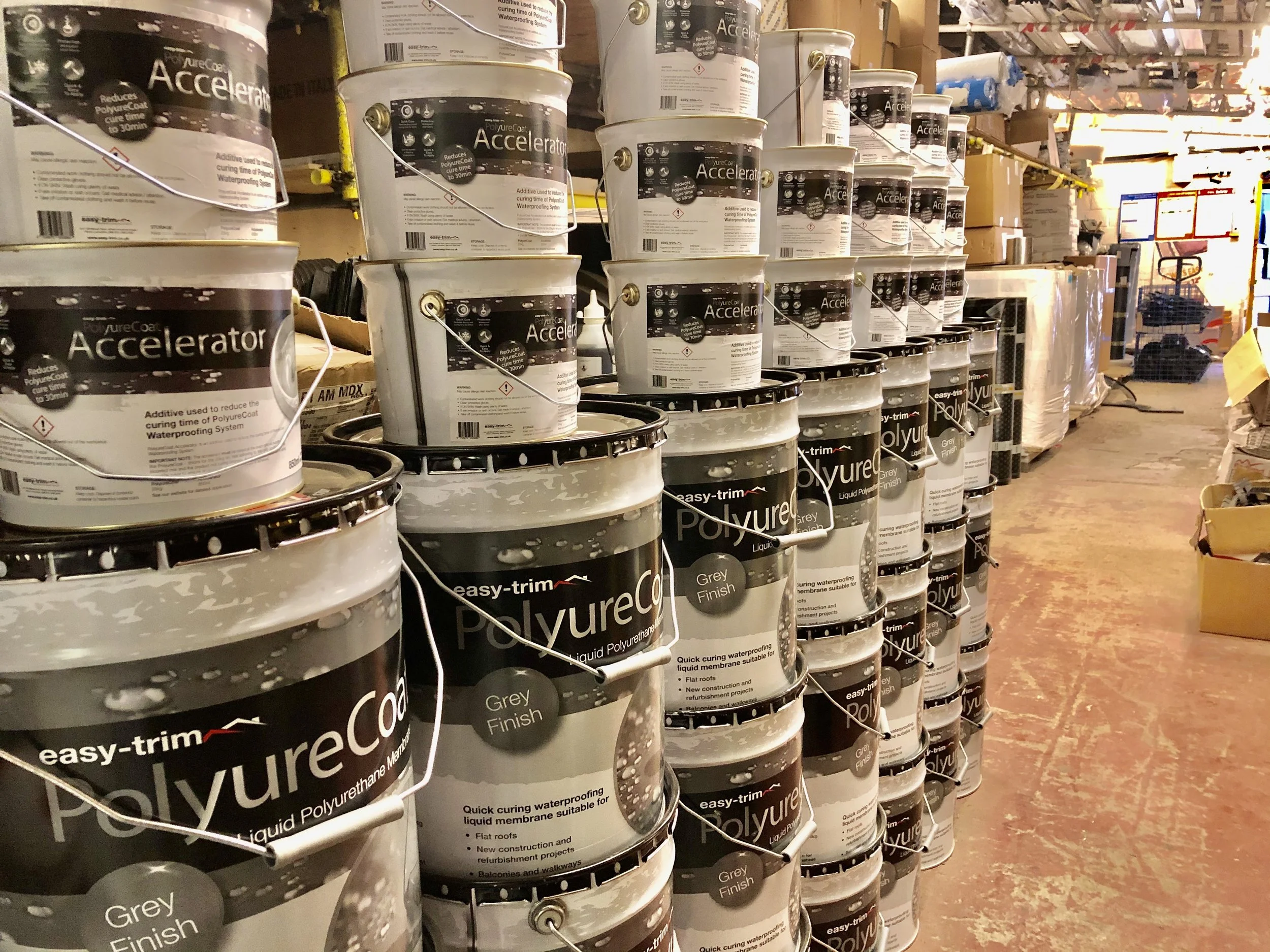Multiple buckets of PolureAttach Polyurea liquid coating in grey finish stacked on store shelves in a hardware or home improvement store.