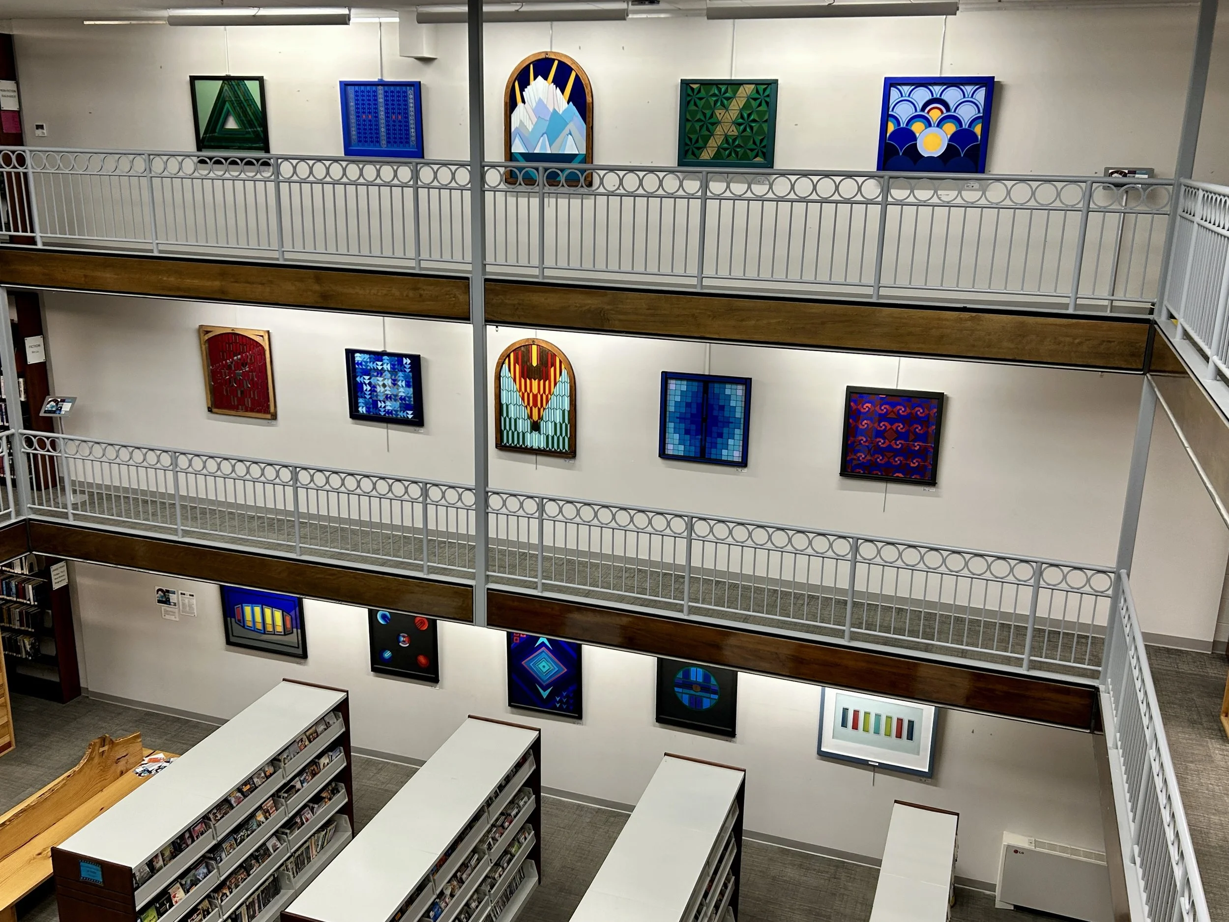 Interior view of an art gallery with paintings displayed on the walls and bookshelves on the lower level.