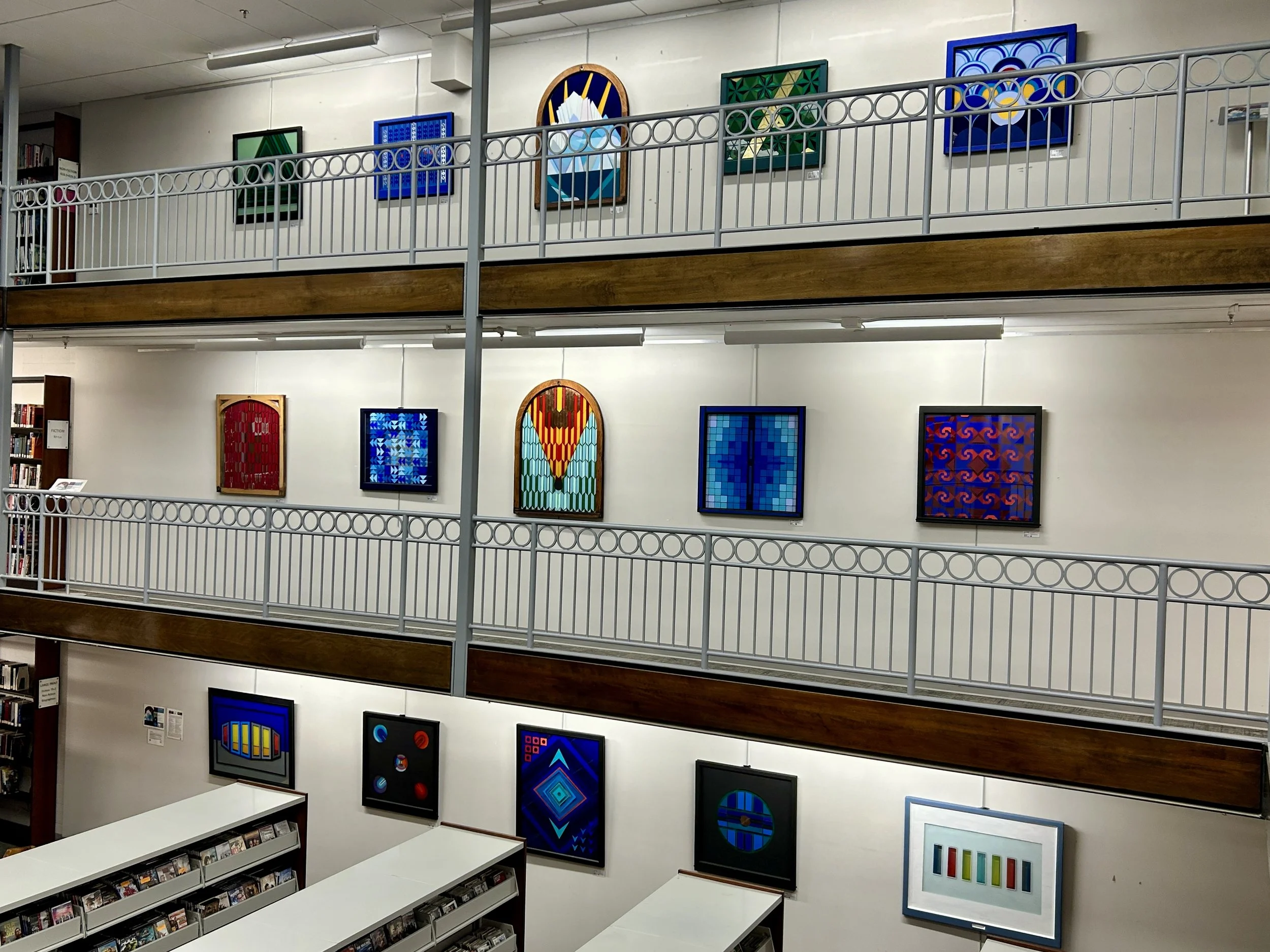 Interior of an art gallery or museum with framed colorful abstract artwork on the walls and shelves with books and DVDs.