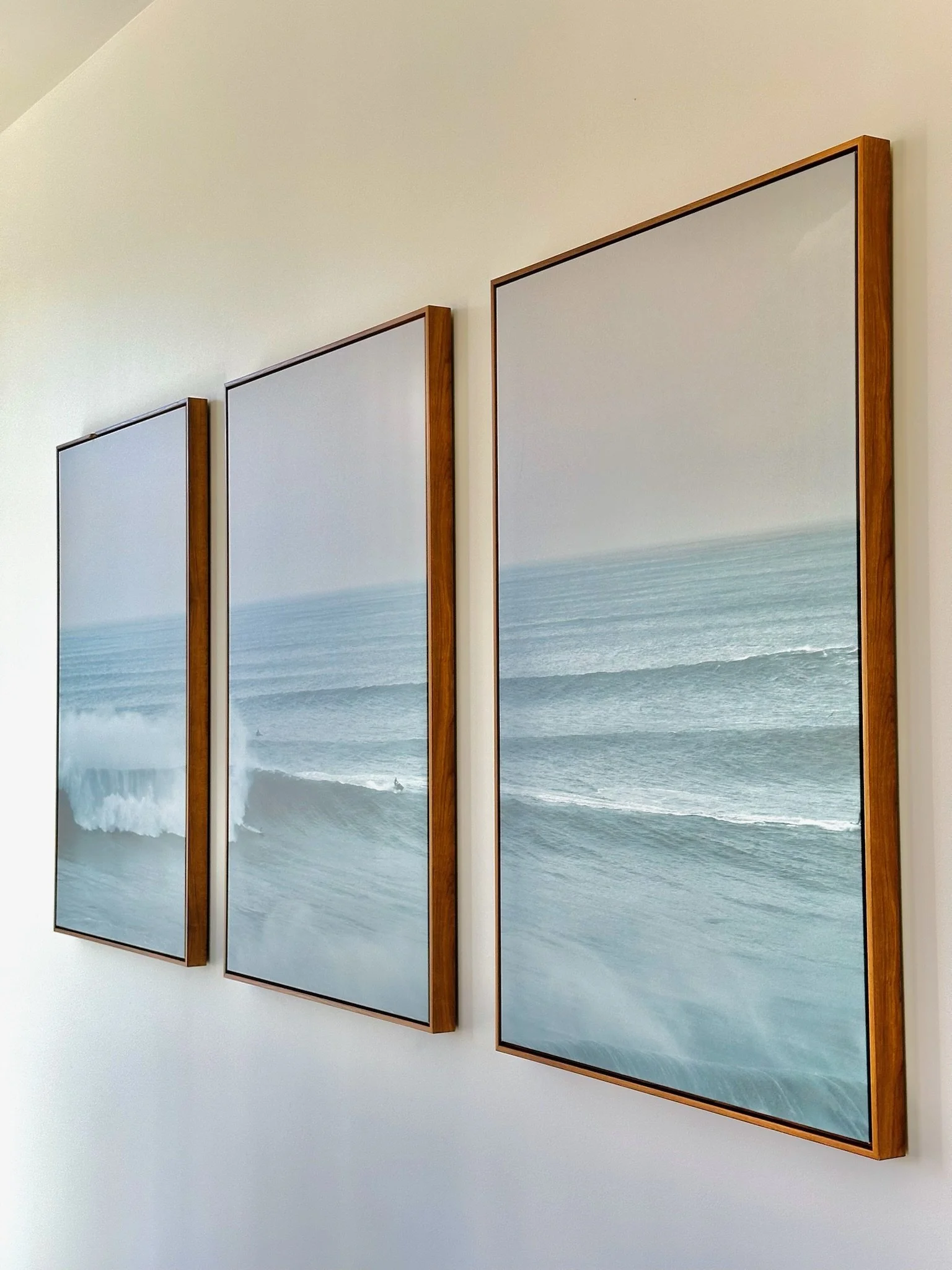 Three vertical panels depicting ocean waves, framed with wood, mounted on a white wall.