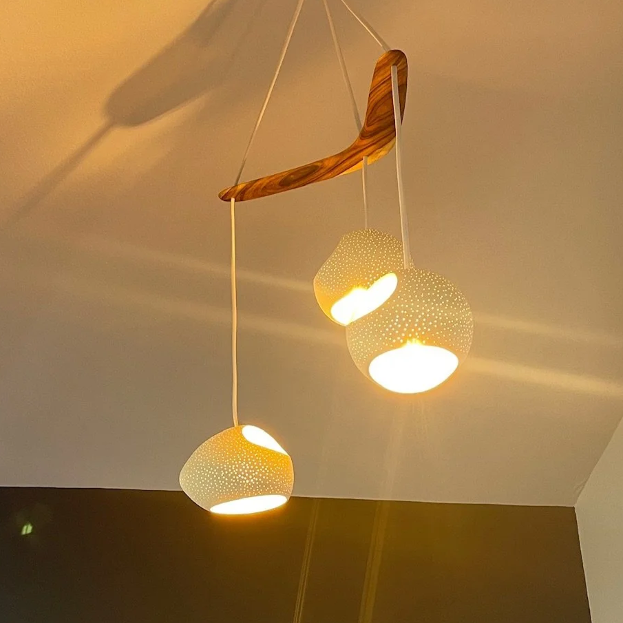 Modern ceiling pendant light fixture with three perforated spherical lampshades hanging from a curved wood and metal mount.