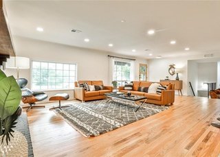 Spacious living room with large windows, orange and beige sofas, a patterned rug, a coffee table, and wooden flooring.