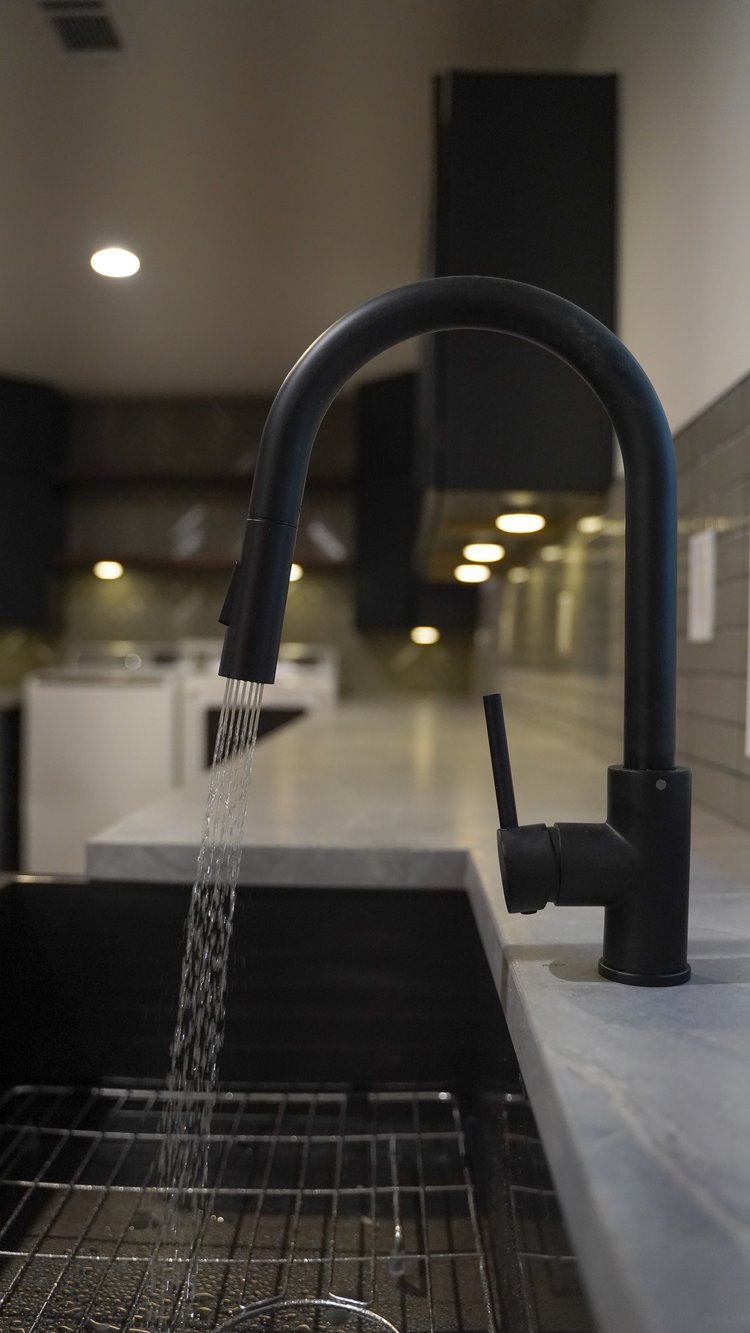 Black kitchen faucet with running water over a stainless steel sink in a modern kitchen.