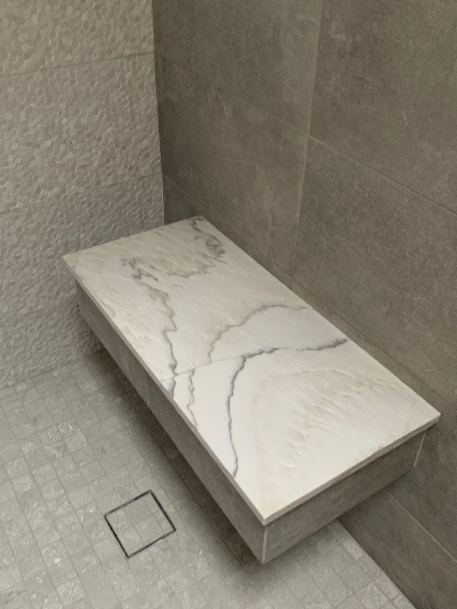 Marble countertop placed on a gray wooden stand in a bathroom with textured wall tiles.