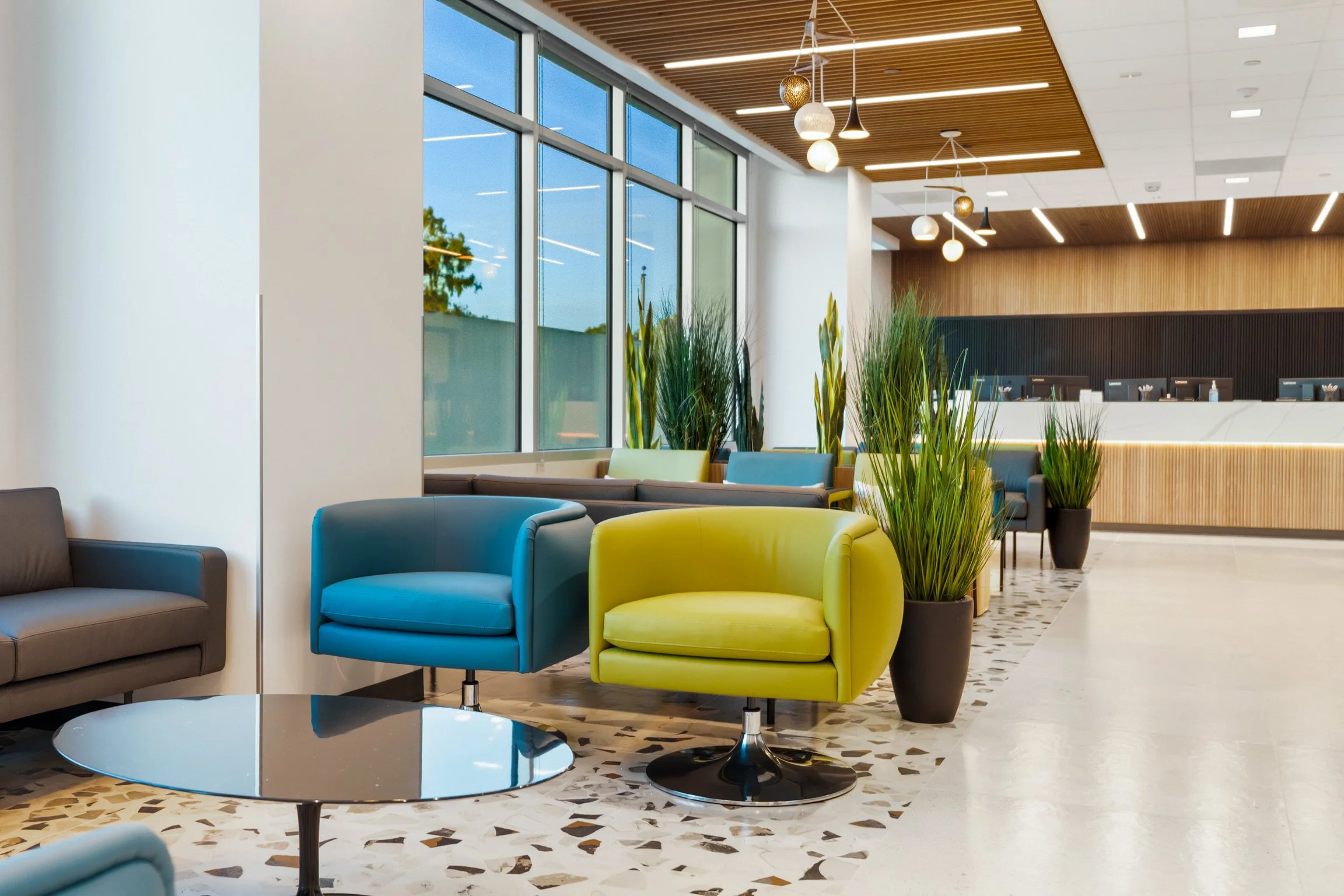Modern lobby with colorful chairs, large windows, indoor plants, and wood-paneled ceiling.
