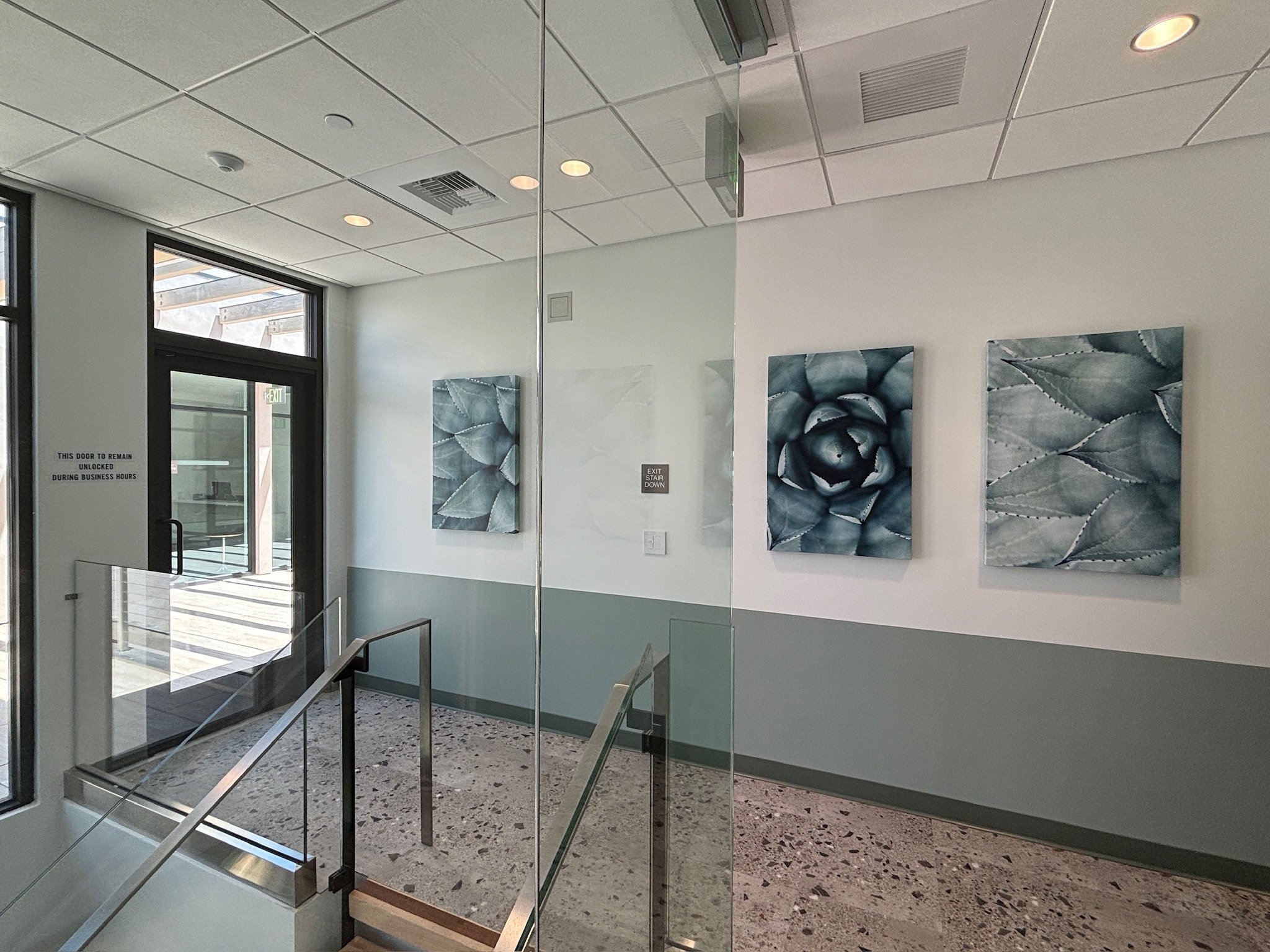 Interior of a modern building with decorative artwork on the wall, glass doors, stairs, and terrazzo flooring.
