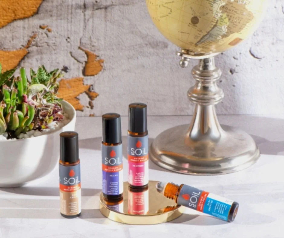 Three bottles of SOiL Organics Remedy Rollers, a globe on a silver stand, and a gold tray on a white surface in front of a textured wall.