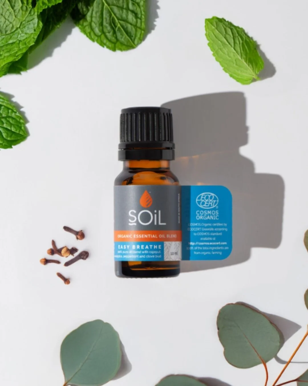 Bottle of Soil organic essential oil blend labeled 'Easy Breathe' surrounded by mint leaves and cloves on a white background.