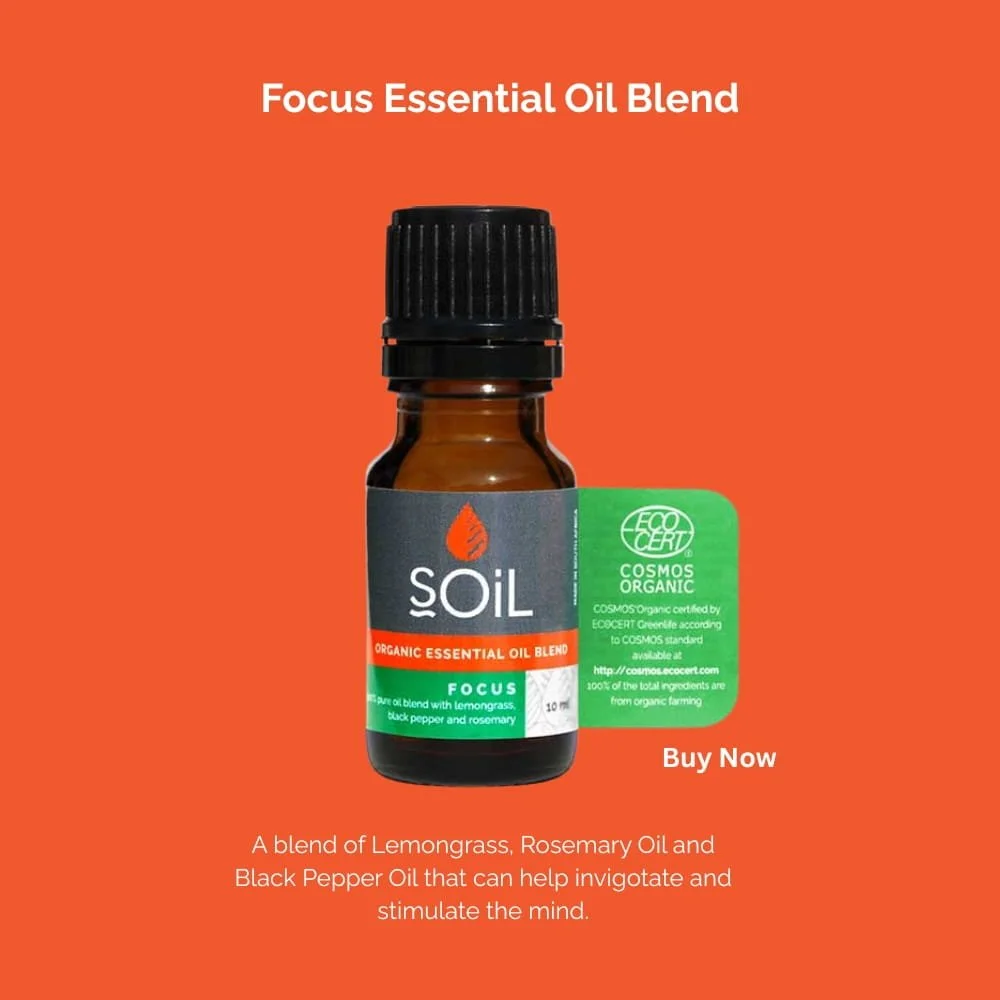 A small amber glass bottle labeled 'Soil Focus Essential Oil Blend' with lemon grass, rosemary, black pepper, and rosemary ingredients, set against an orange background. A green eco-cert label is attached to the bottle. The image promotes a blend of organic essential oils designed to help invigorate and stimulate the mind with a 'Buy Now' prompt.