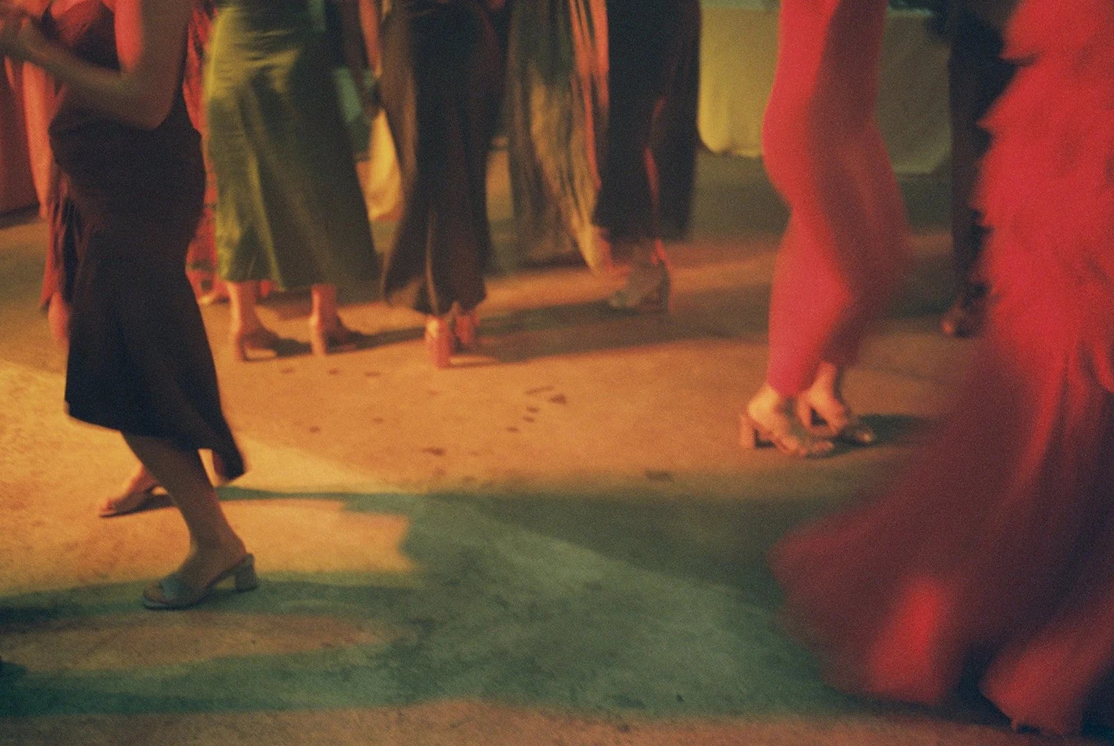 Women dancing on a dimly lit dance floor, wearing colorful dresses and heels.
