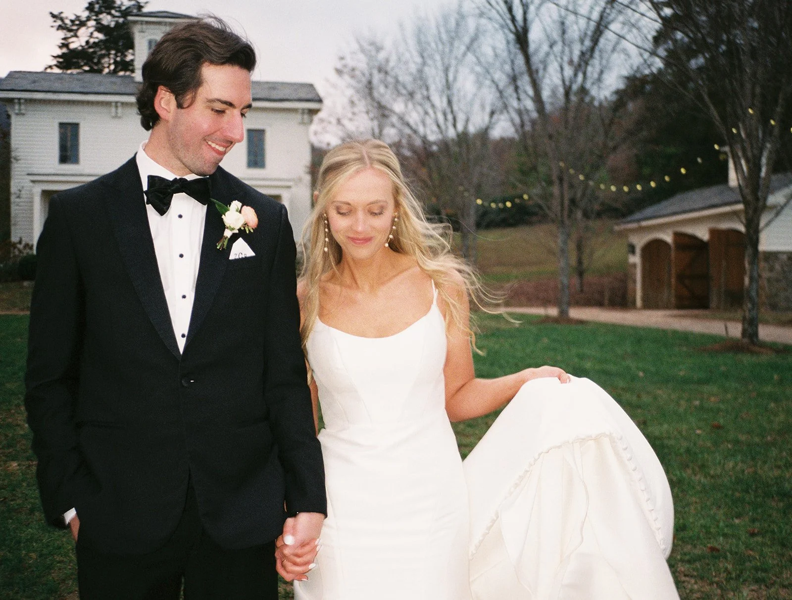 A bride and groom walking outdoors on their wedding day, holding hands.