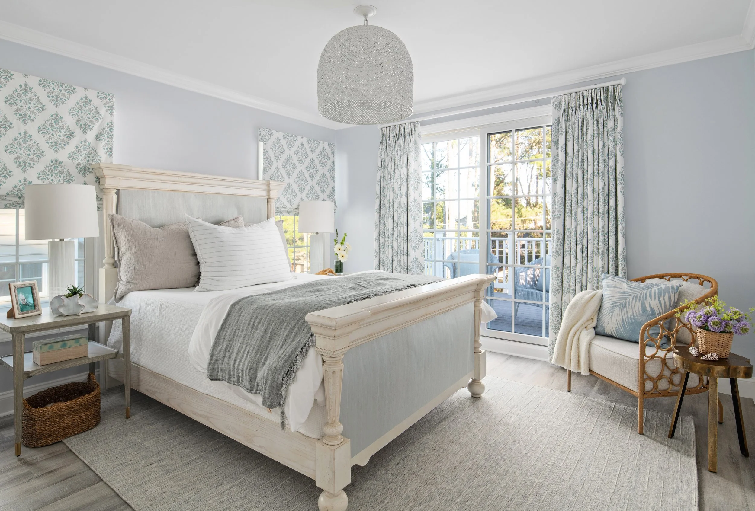 Bright bedroom with white bed, patterned curtains, and balcony door, decorated in light, neutral tones with wicker and floral accents.