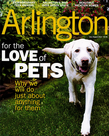 A white dog running on green grass in a park with trees in the background on the cover of Arlington magazine.