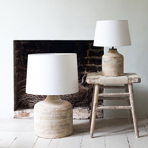 Two rustic table lamps with white shades placed on a wooden stool in front of a vintage fireplace.