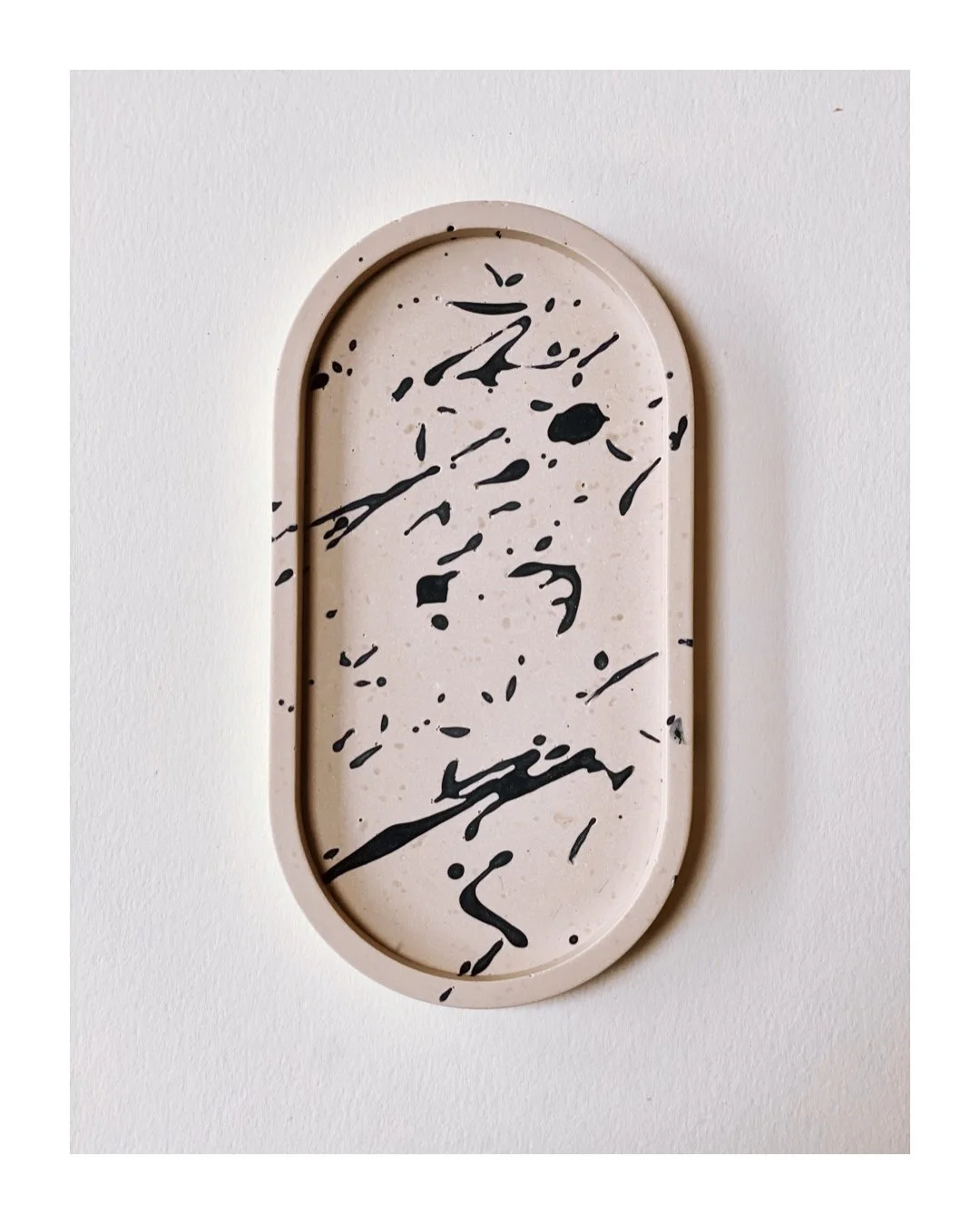Oval beige tray with black paint splatter design on a white background.