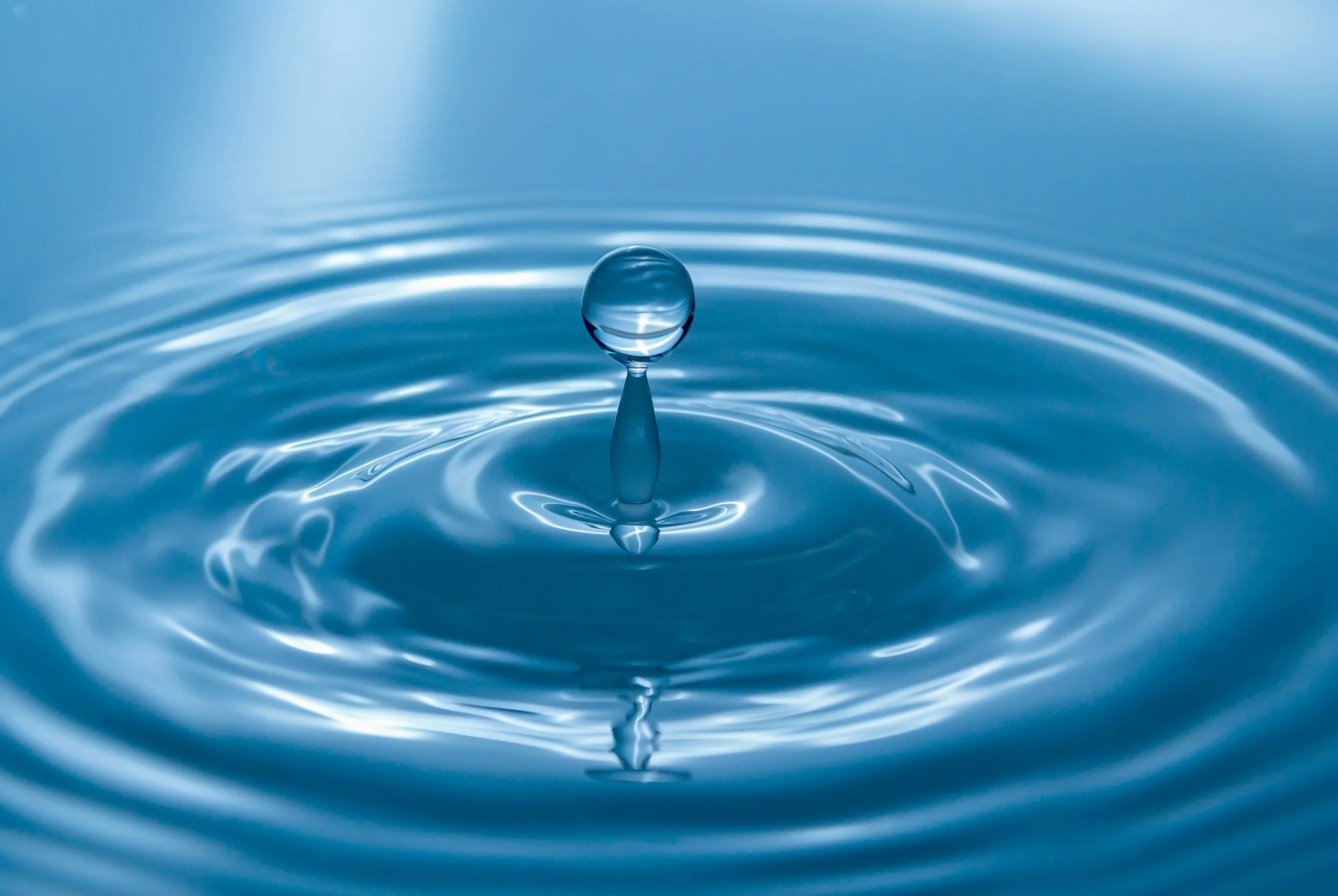 Close-up of a water droplet hitting a calm water surface, creating ripples.