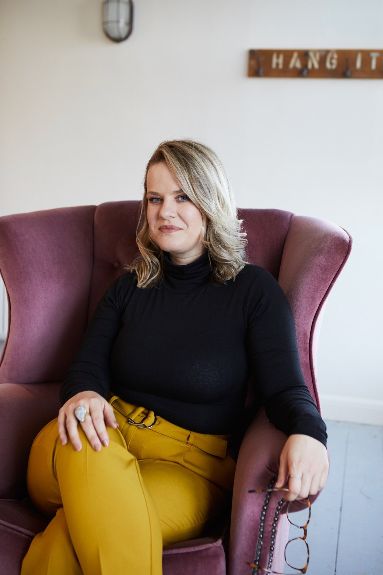 Cherish Amber sex and relationship coach sitting in pink velvet wingback chair smiling warmly.