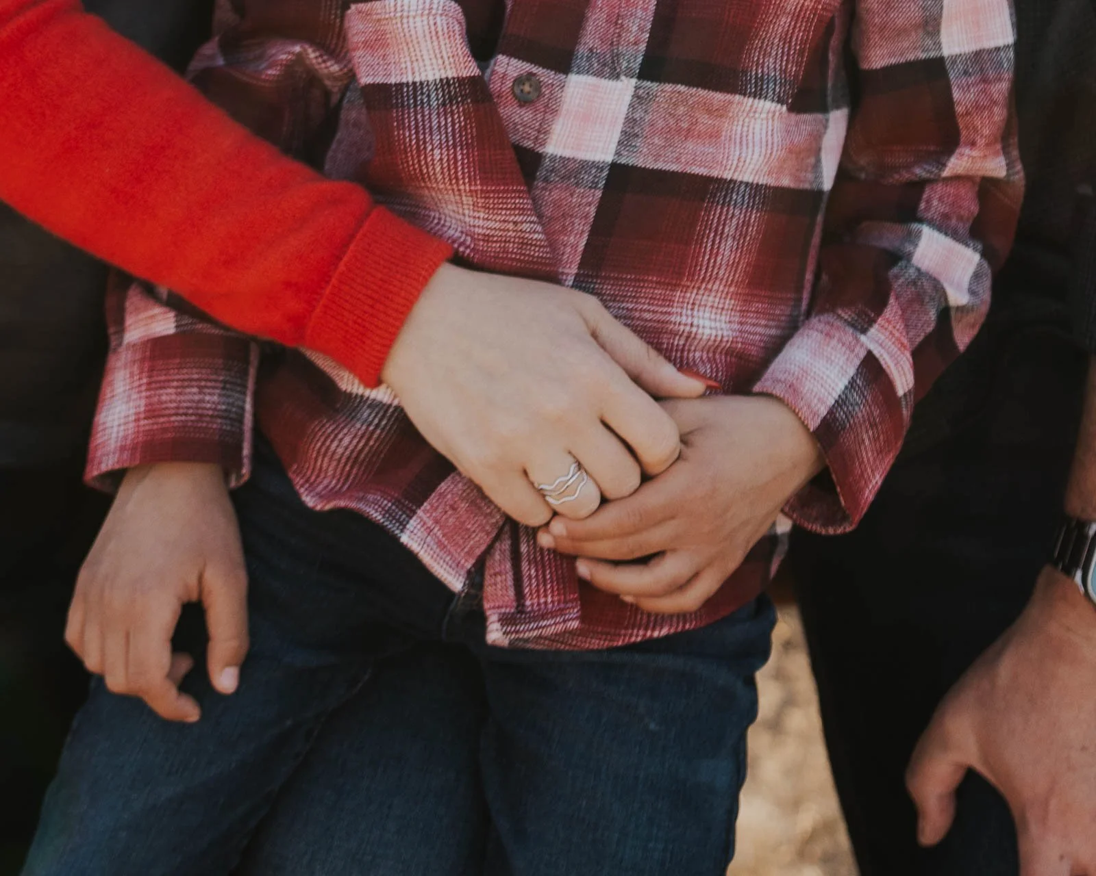 mom and dad clasp hands in front of son hugging him in close