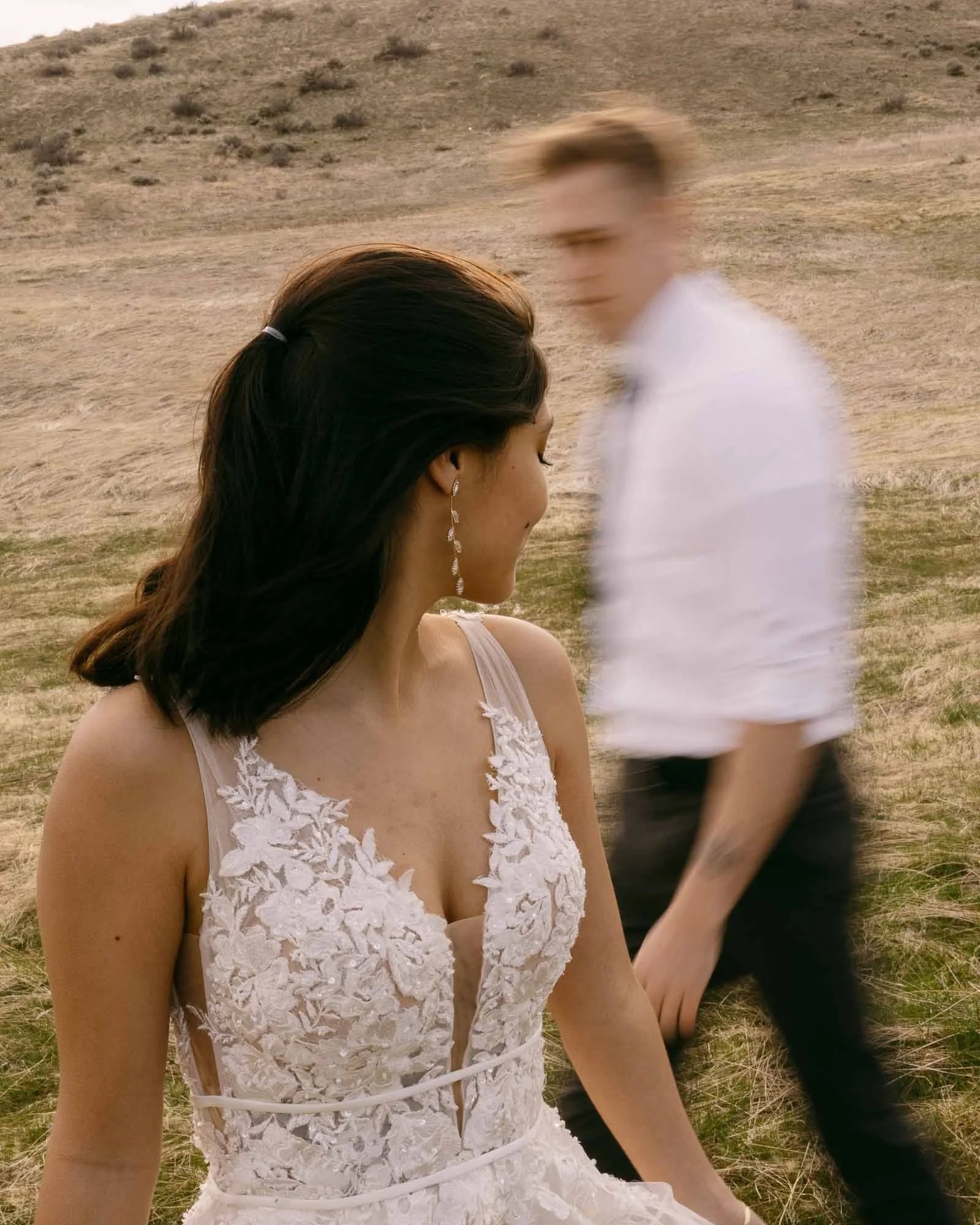 The groom walks behind the bride so quickly he is blurry. The groom’s silhouette fits artistically in the space left from the bride’s torso. The bride is looking at the groom while he walks by