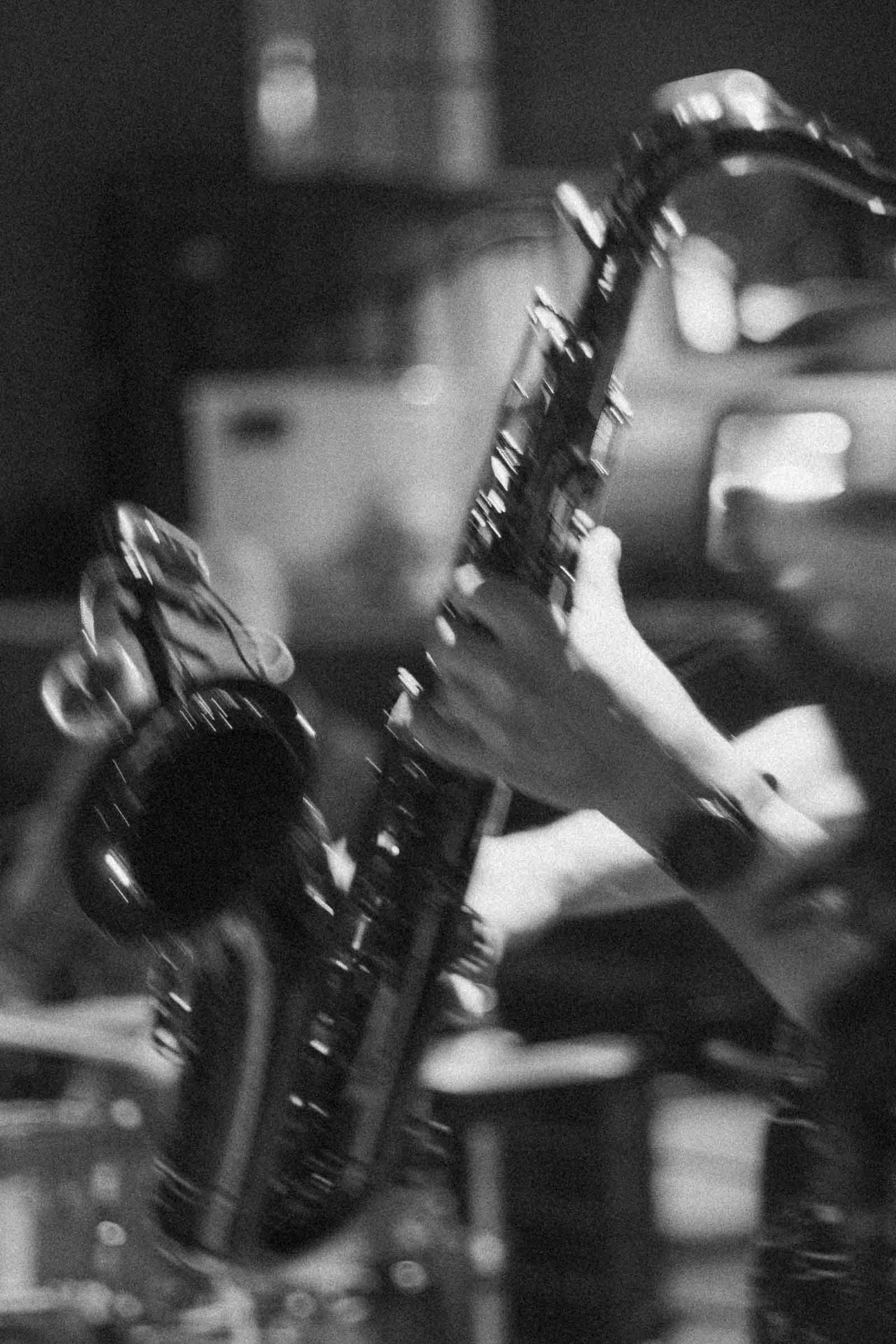  Black and white image of a person playing a saxophone. The focus is on their hands holding the instrument, with a blurred background suggesting a live music setting. 