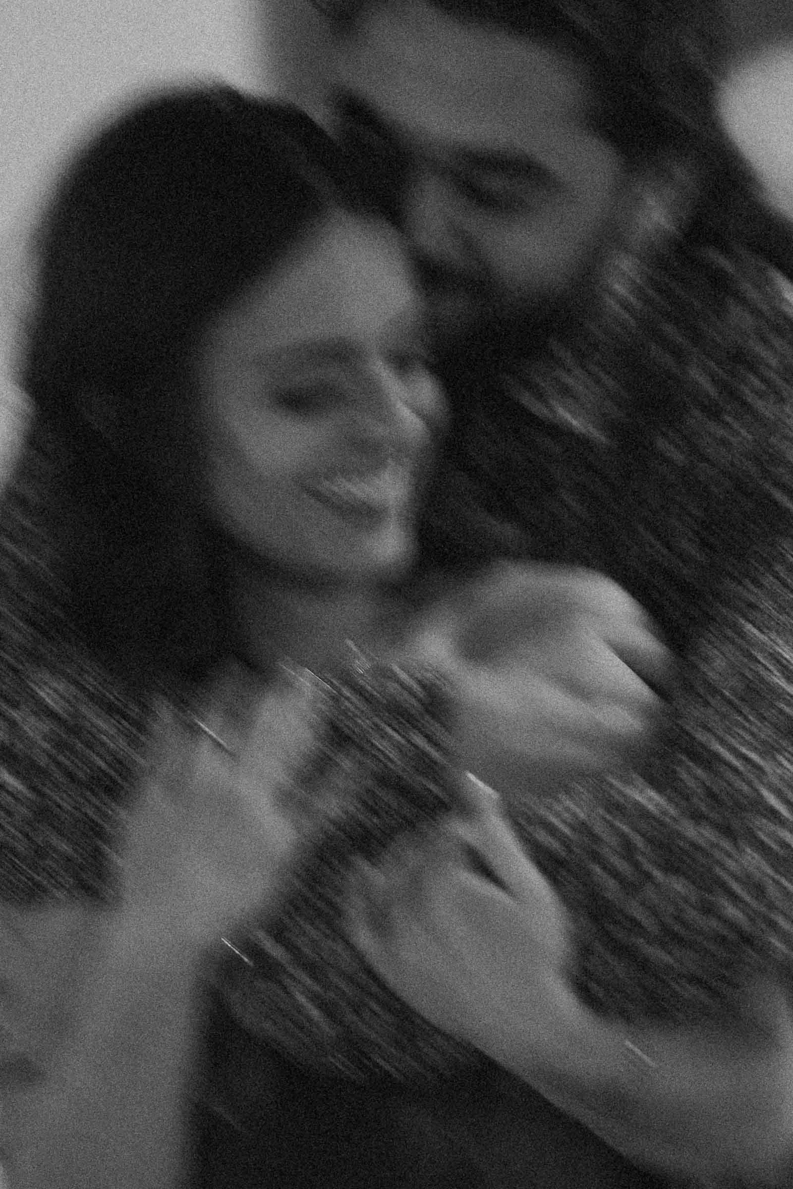 A black and white, blurry photo of a couple embracing and smiling, capturing a joyful and affectionate moment between them.