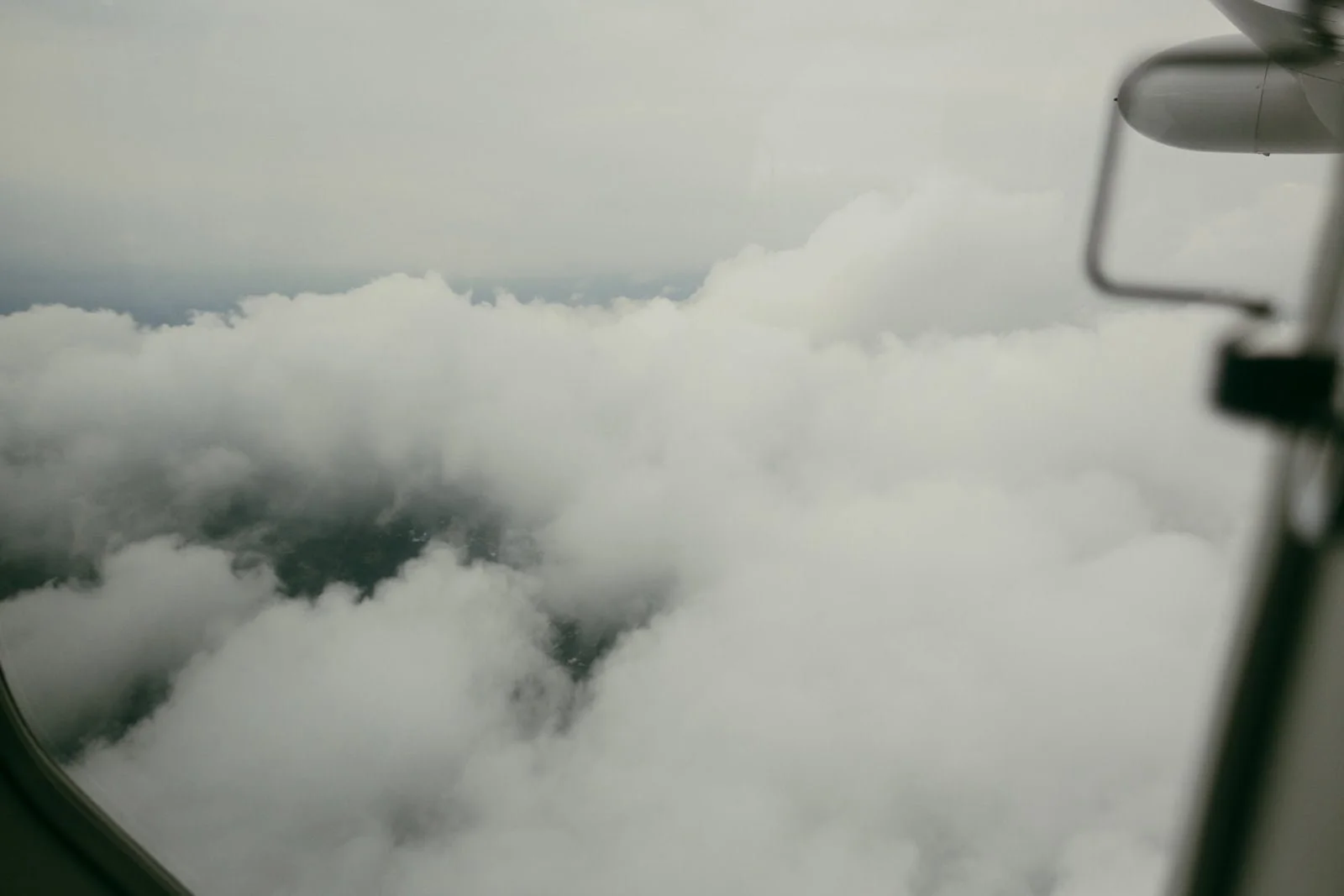  A view from an airplane window showing thick white clouds below and the airplane wing partially visible on the right side. 