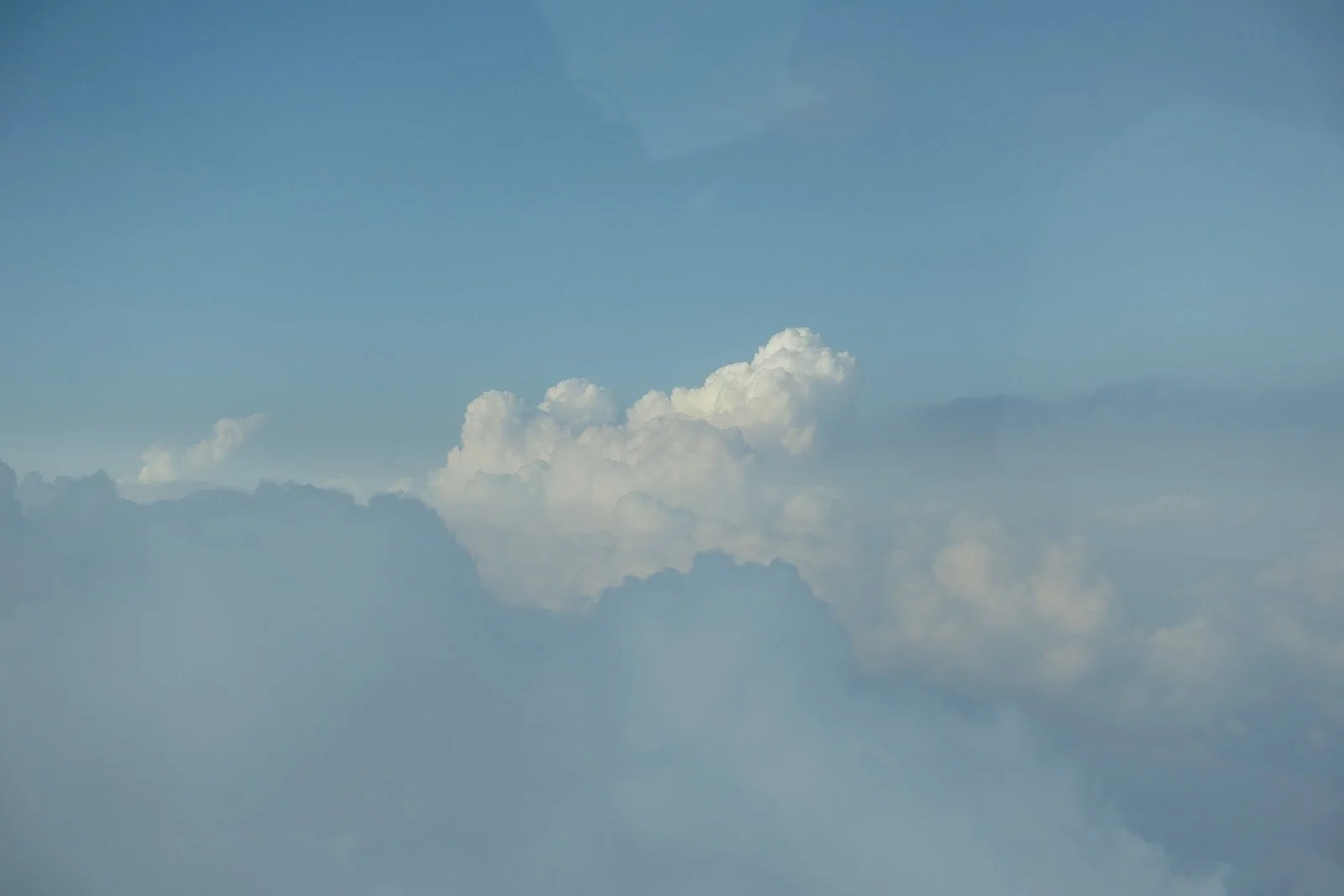  Blue sky with fluffy white clouds viewed from above, suggesting the photo was taken from an airplane. The sunlight softly highlights the tops of the clouds, creating a serene and peaceful atmosphere. 
