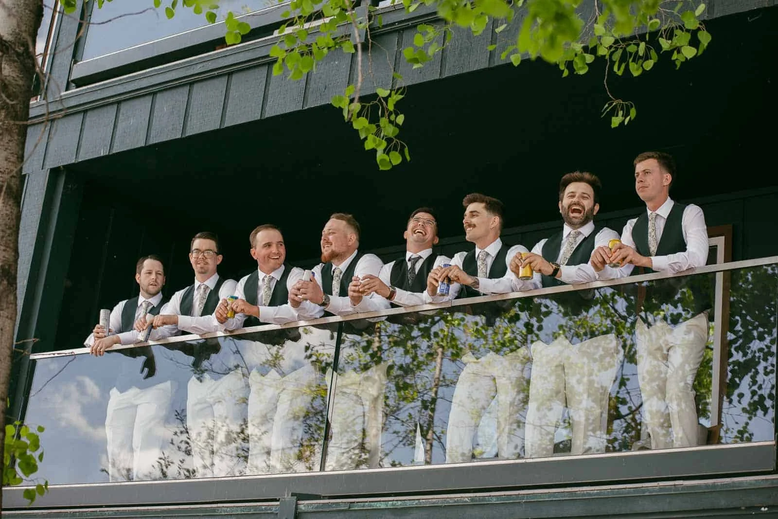  Eight men dressed in white shirts, vests, and ties stand smiling on a balcony, each holding a yellow-green apple, with green leaves visible in the foreground. 