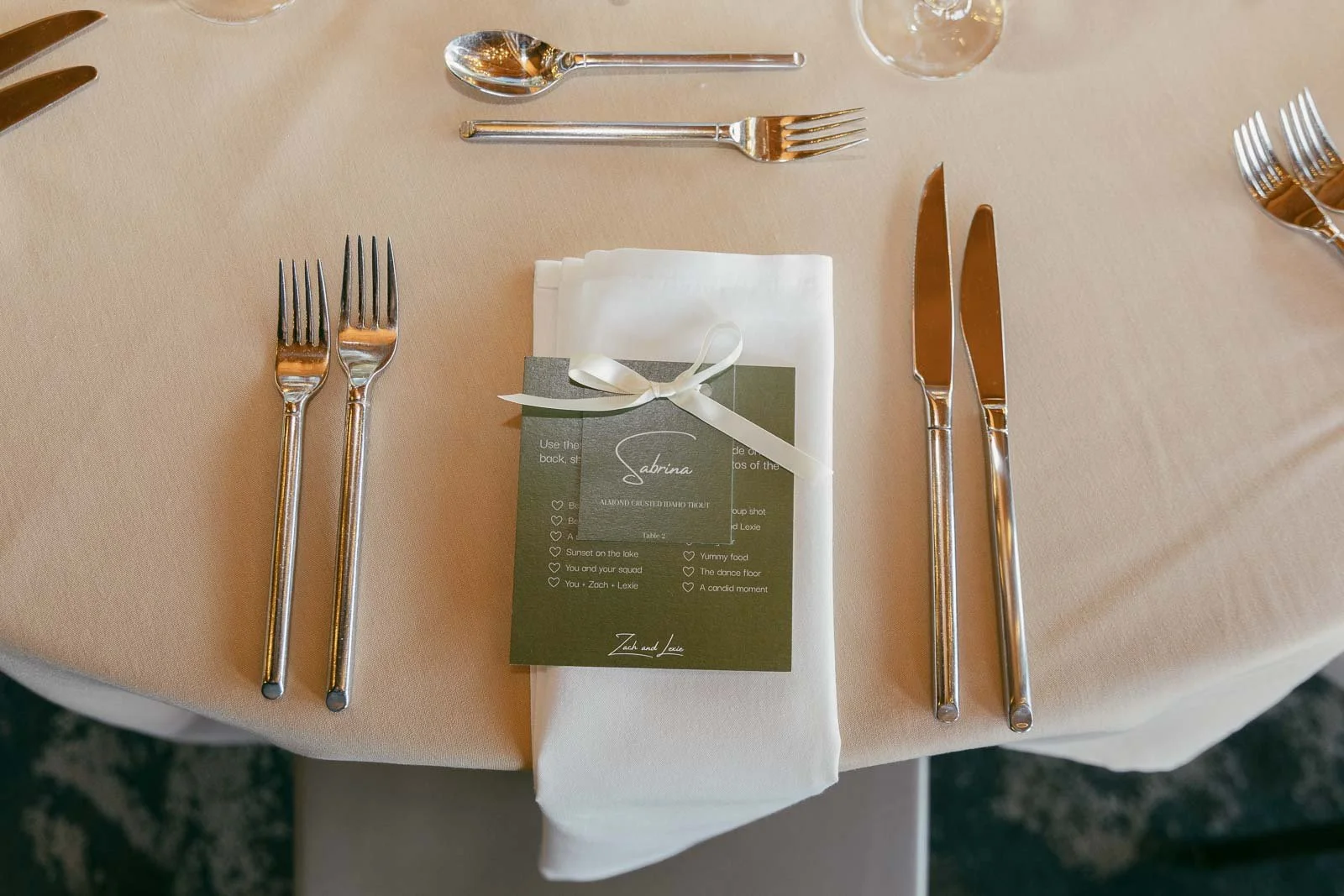  A formal table setting with forks on the left, knives and a spoon on the right, and a folded white napkin in the center tied with a ribbon and a green menu card placed on top. 